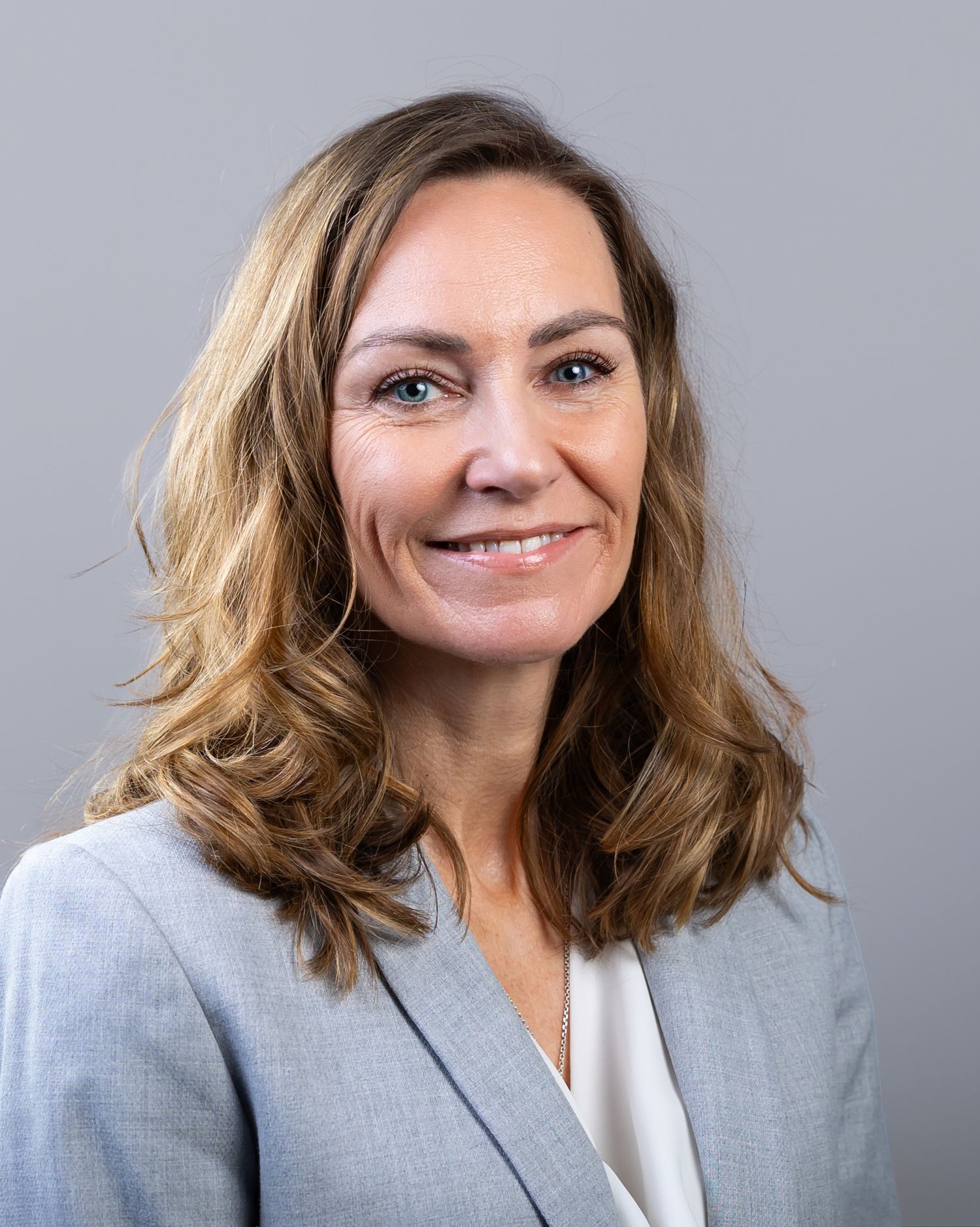 Professional headshot series showing someone in a gray blazer with wavy shoulder-length hair against a neutral background.