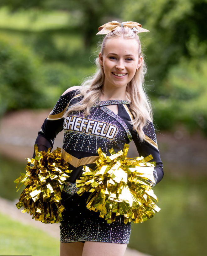 Cheerleader in sparkly Sheffield uniform holding gold pom poms outdoors.