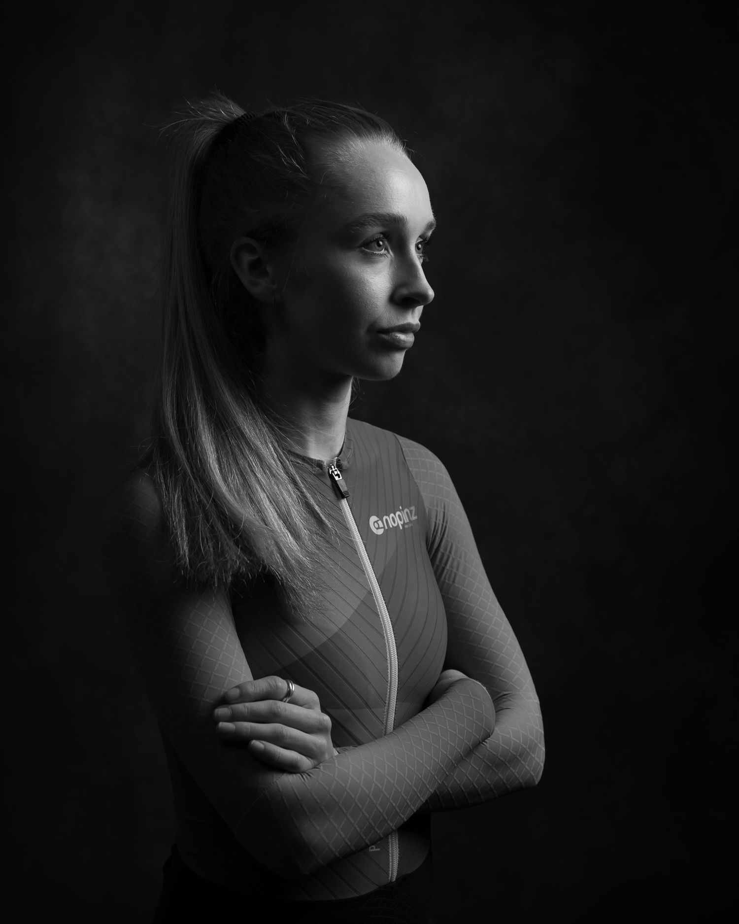 Dramatic black and white portrait of an athlete in profile view with crossed arms, illuminated against dark background.