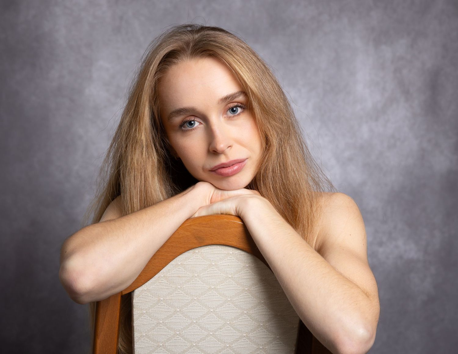 Portrait of someone resting on a chair back against gray background with soft lighting and natural expression.
