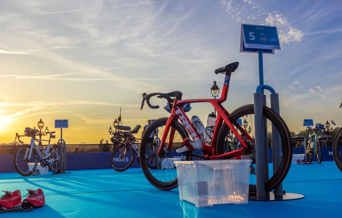 Red racing bike staged at transition area during sunset at triathlon event.