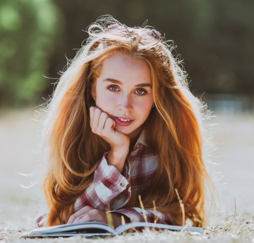 Portrait of person reading book outdoors in plaid shirt with sunlit hair.