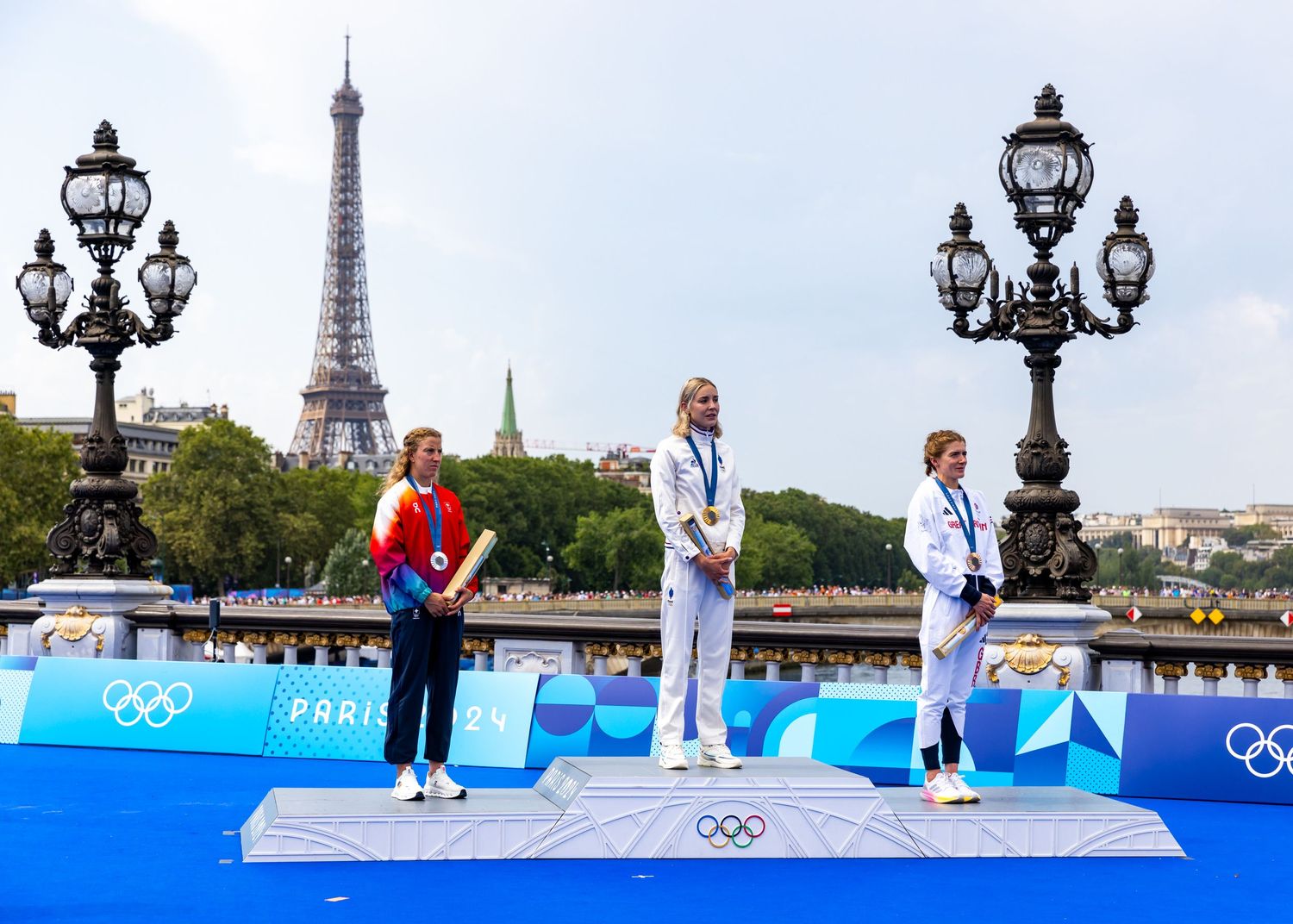 Olympic medalists stand on a podium with the Eiffel Tower visible in the background.