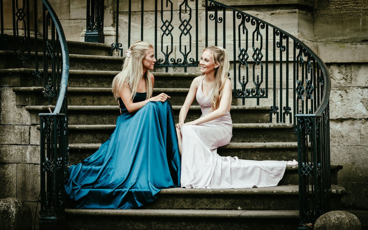 A romantic couple sits on stone steps with the bride wearing a flowing blue dress and white gown.