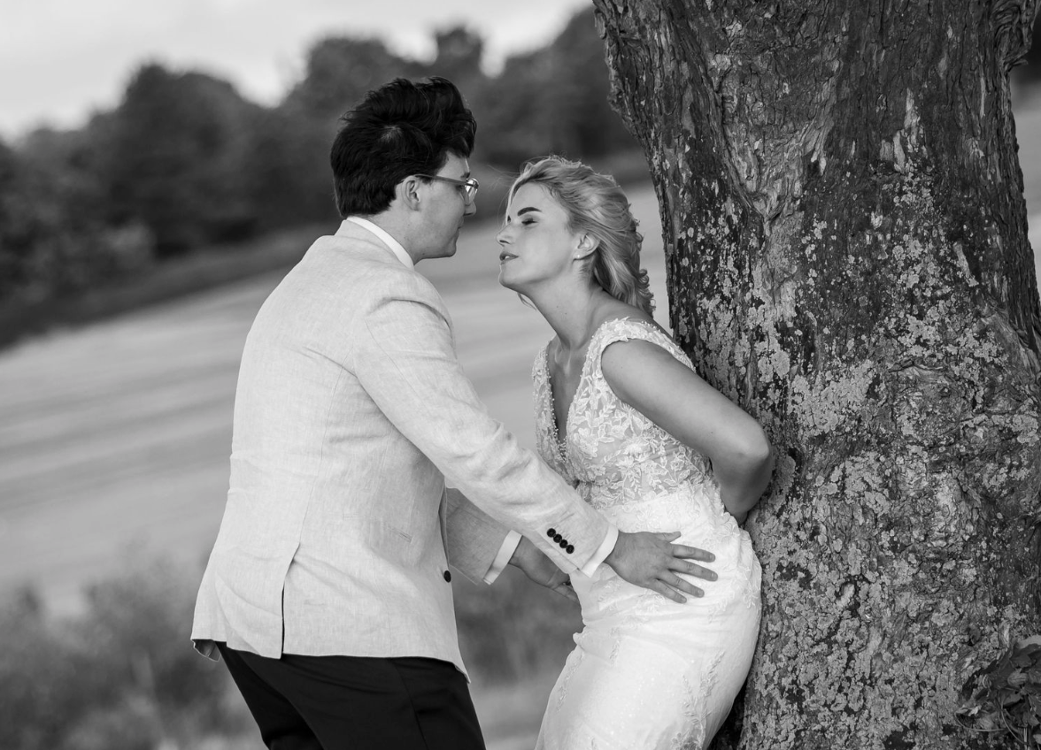 A romantic black and white portrait of a couple embracing against a tree.