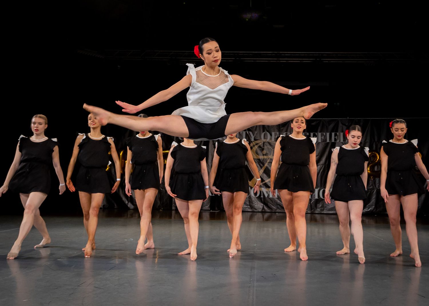A dance performance with performers in black costumes as one dancer leaps into a dramatic split pose.
