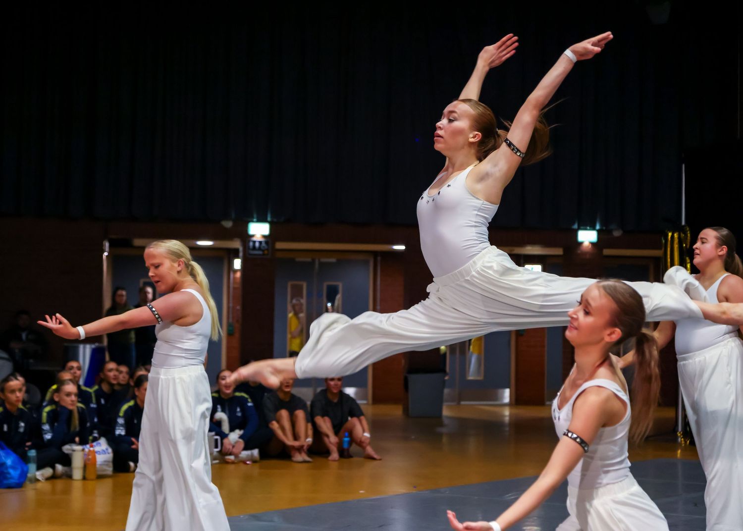 Modern dancers in white costumes perform leaps and choreographed movements on stage.