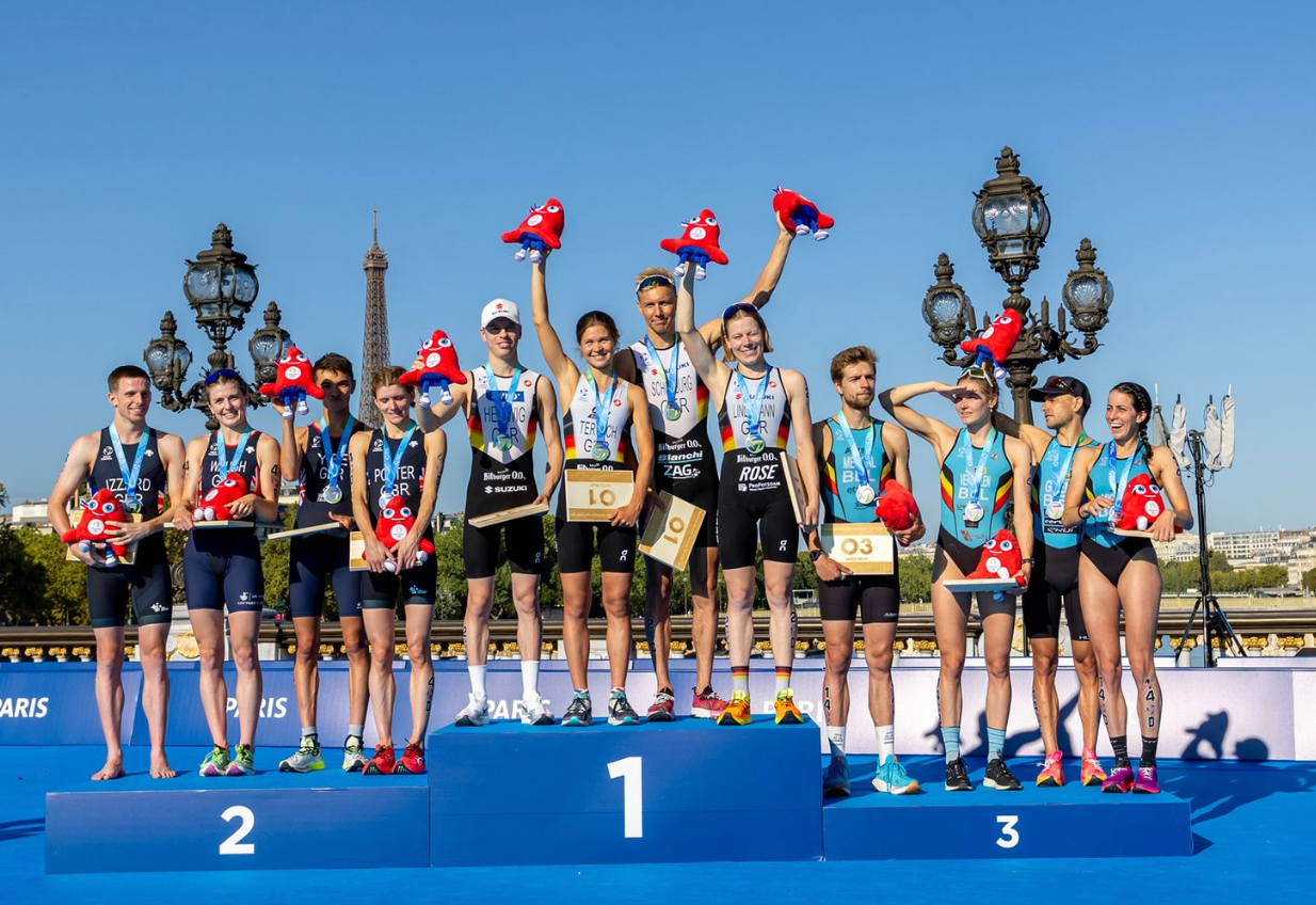 Athletes celebrating on a tiered podium with the Eiffel Tower visible in the background.