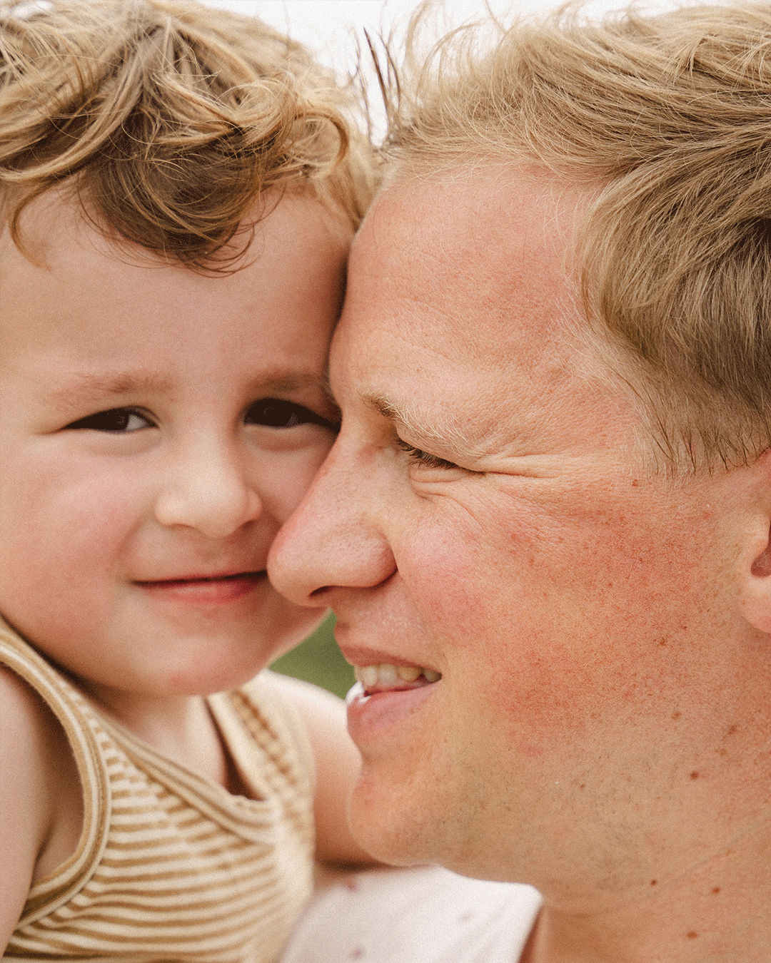 Photoshoot of dad and son portrait on father’s arm in a calm, minimalist setting in nature. / Fotoshoot vader en zoontje in de natuur.