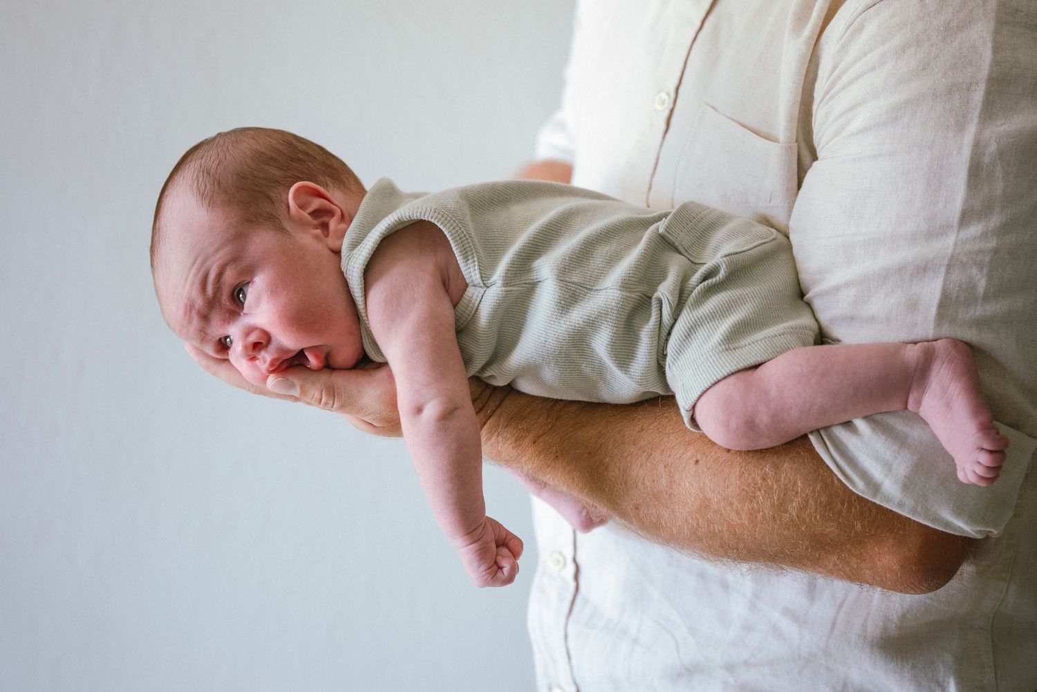 Natural newborn portrait of baby resting on father’s arm in a calm, minimalist setting. / Natuurlijk newbornportret van baby die rust