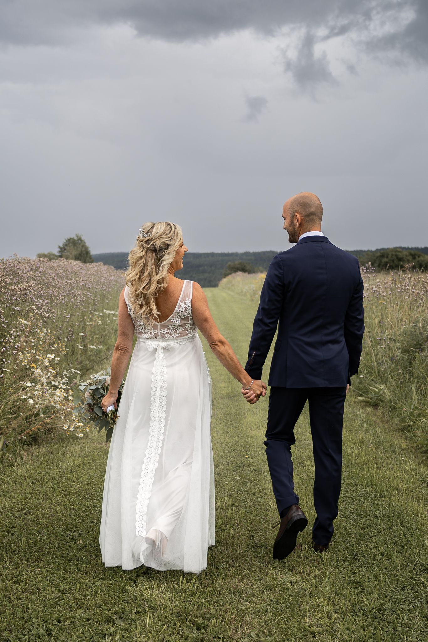 Brudpar går hand i hand genom en blommande äng på bröllopsdagen