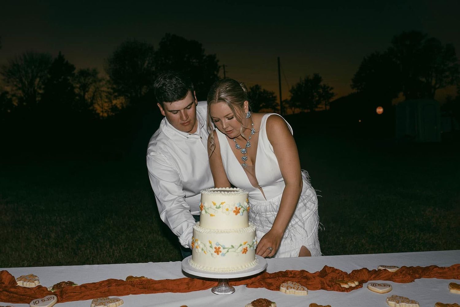 Wedding cake cutting scene at dusk with soft lighting and romantic ambiance.