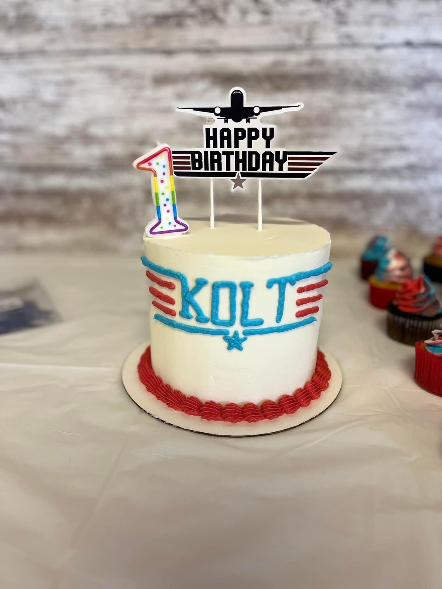 A white frosted cake with aviation theme decorations including a plane silhouette and blue accents.