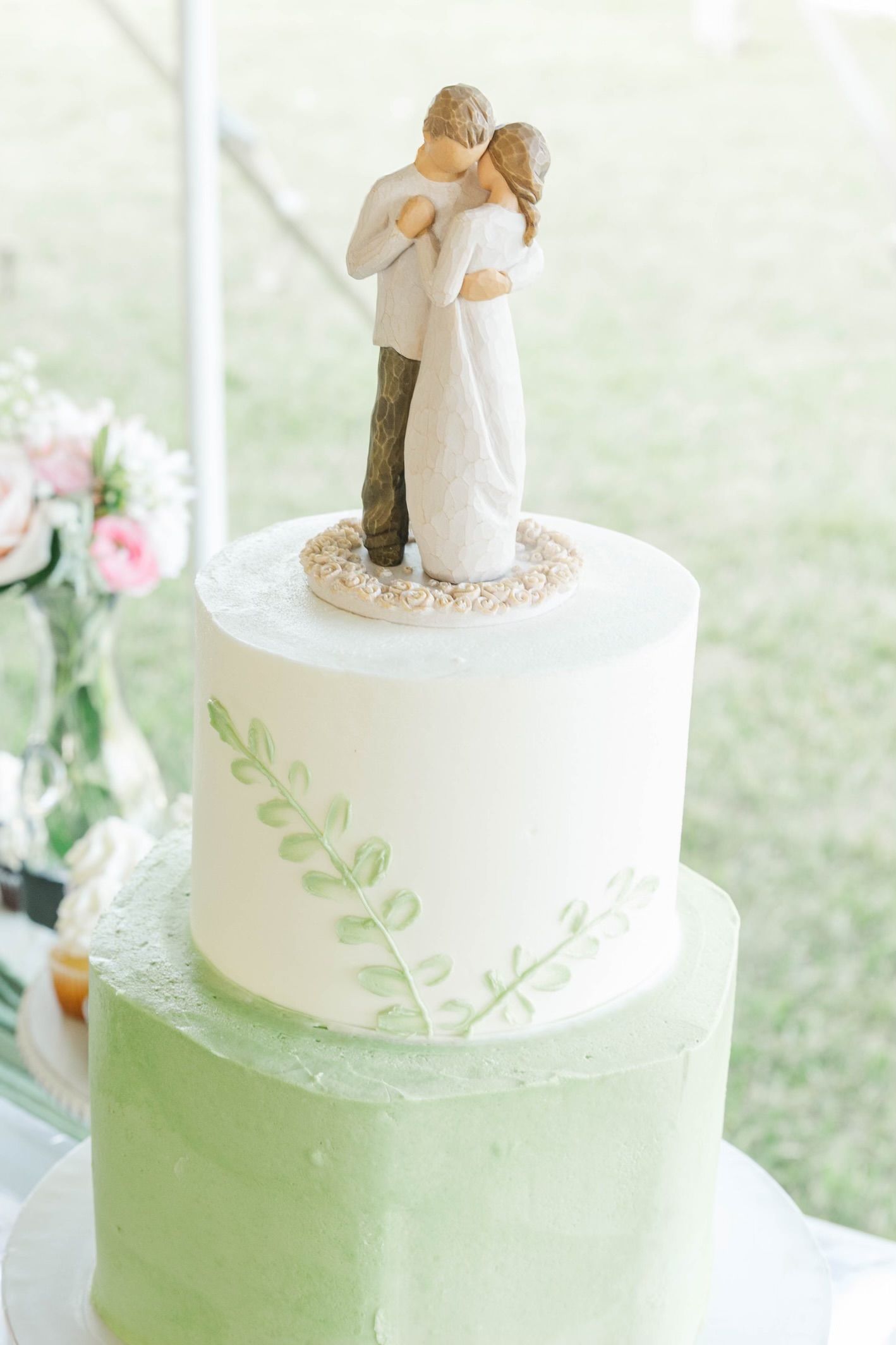 Two-tiered mint green and white wedding cake with delicate leaf details and figurine topper.
