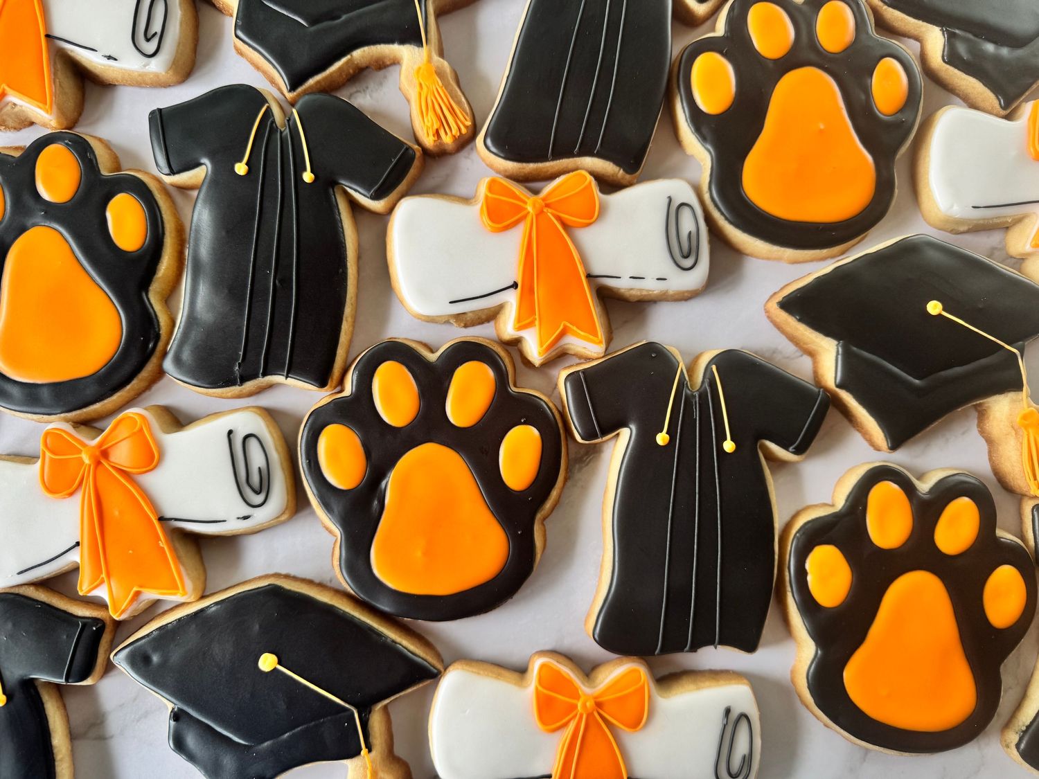 Black and orange decorated cookies featuring paw prints and graduation caps.