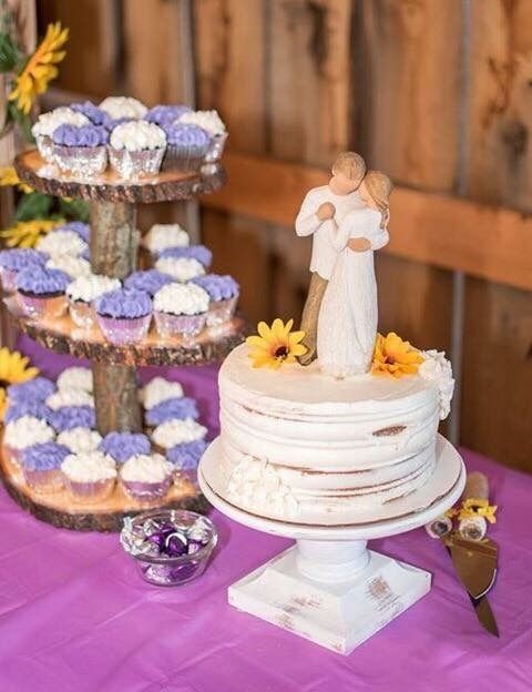 Wedding cake display on purple tablecloth with rustic wood stands and purple floral decorations.
