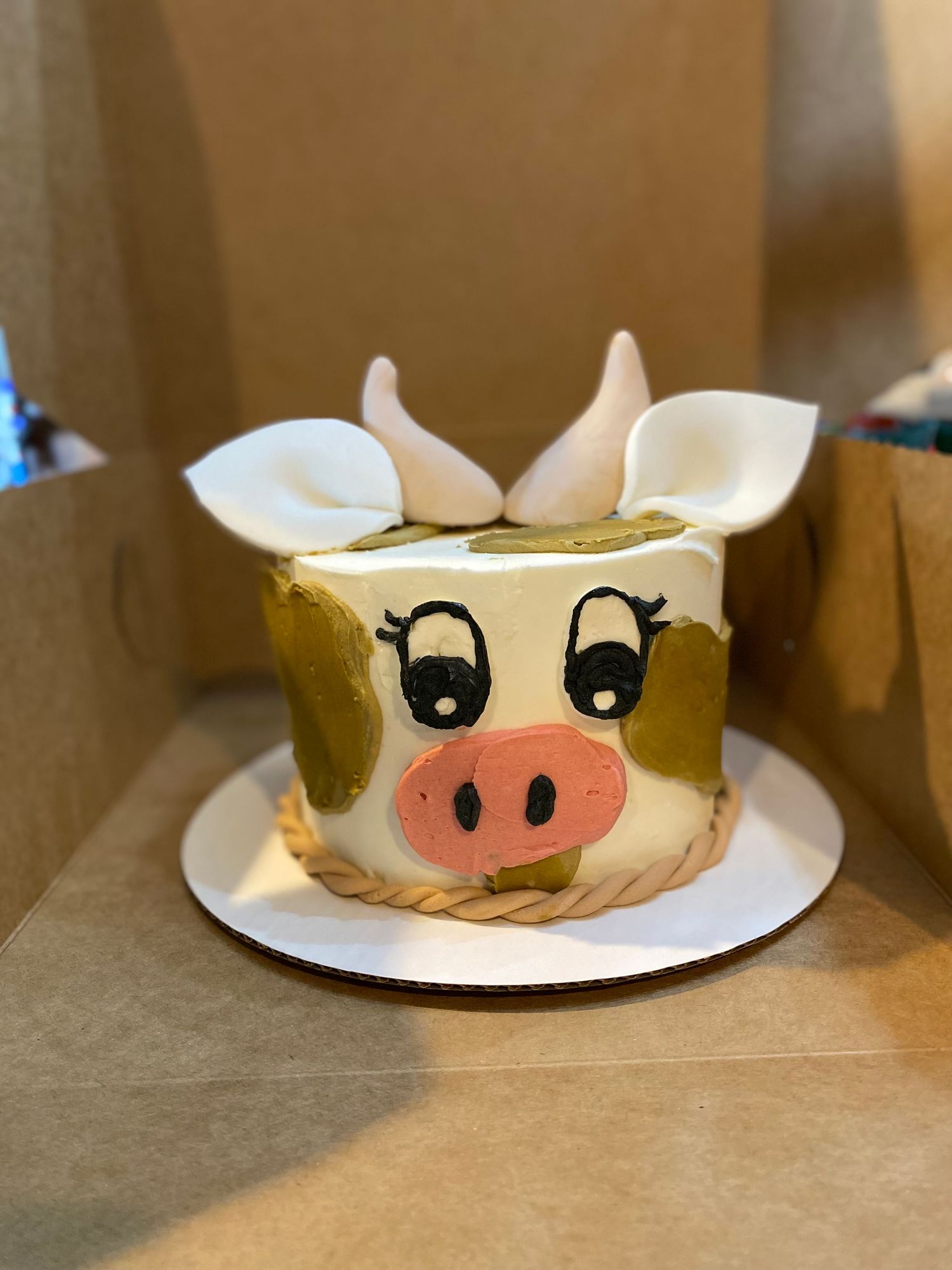 Round cake decorated to look like a cute cow face with pink nose and black eyes.
