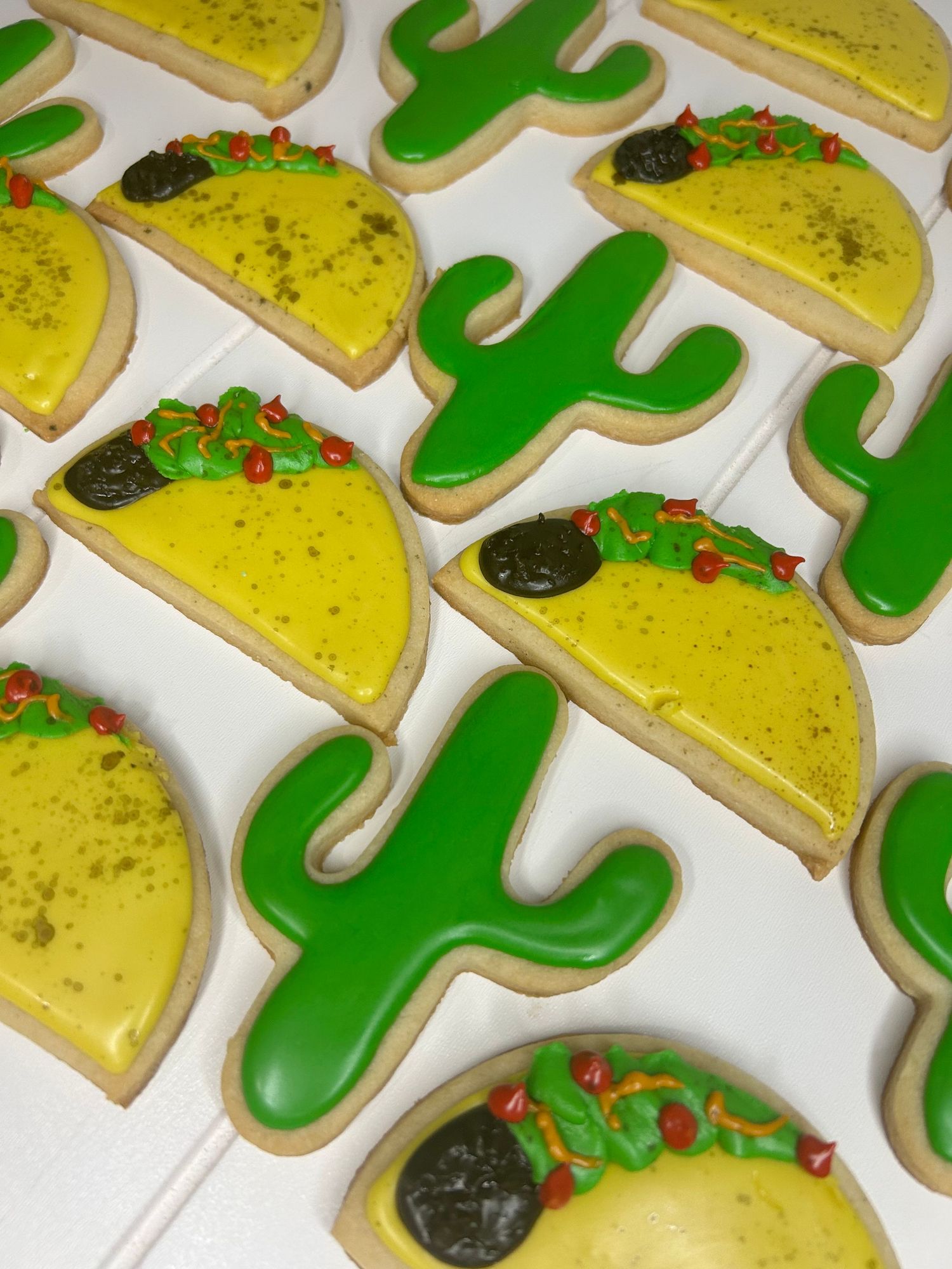 Decorated sugar cookies with yellow and green cactus designs arranged in neat rows.