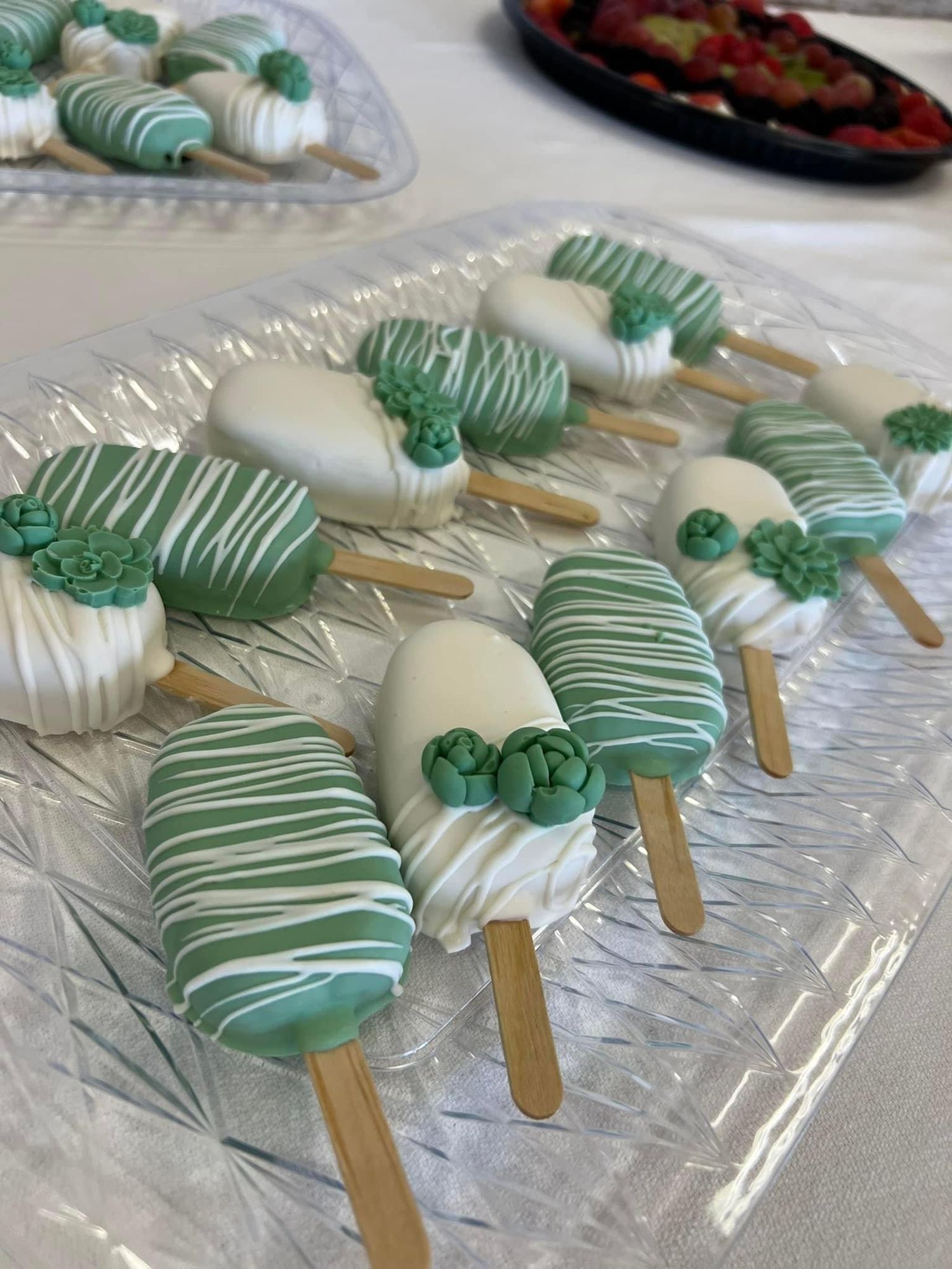 Mint green and white chocolate-covered cake pops arranged on a clear serving platter.