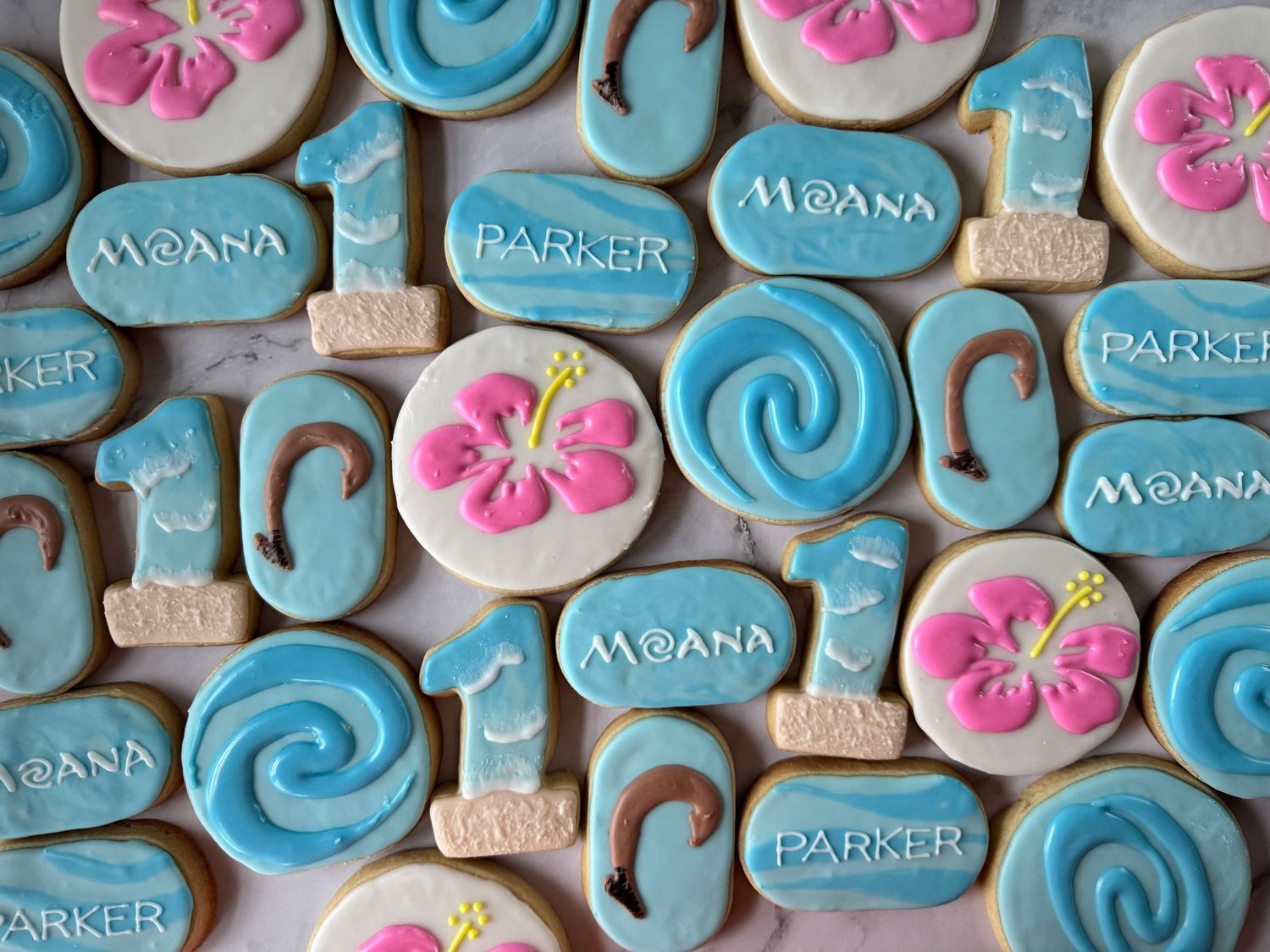 Collection of blue and pink themed Moana sugar cookies with tropical flower designs.