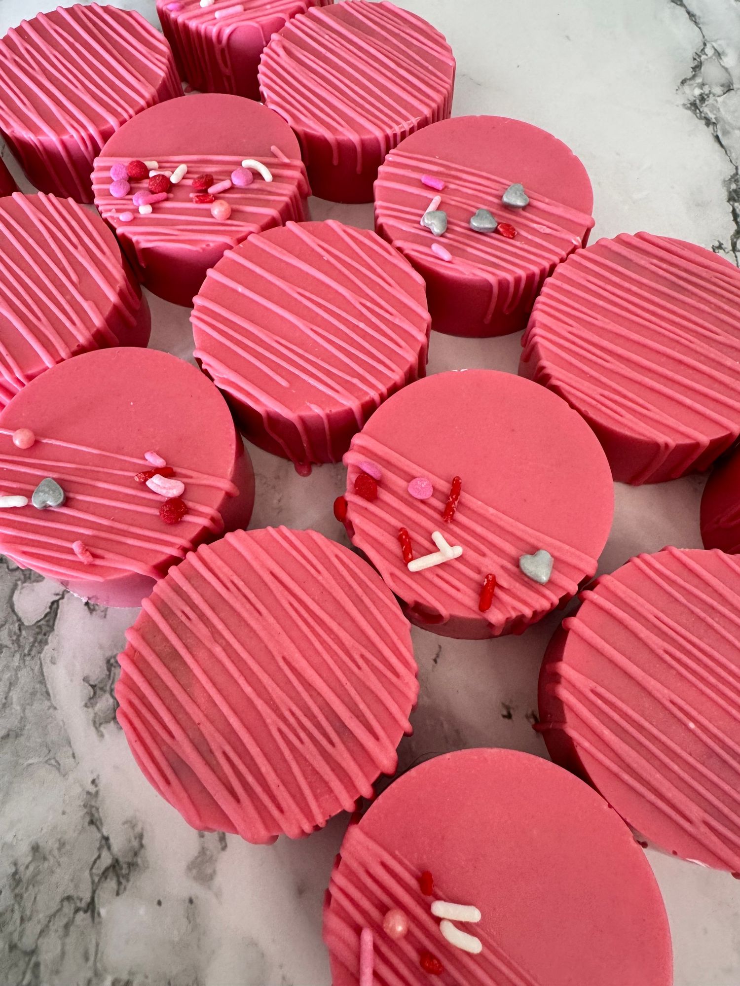 Pink heart-shaped chocolate covered treats with white drizzle arranged on marble countertop.