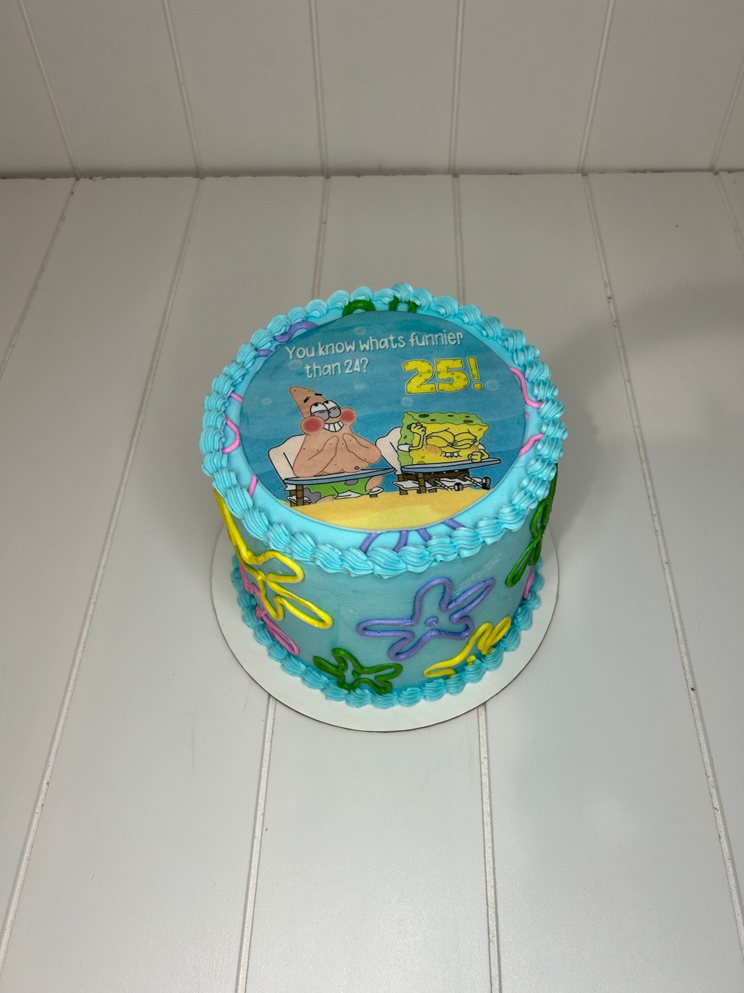 A light blue birthday cake decorated with SpongeBob SquarePants themed designs and the number 25.