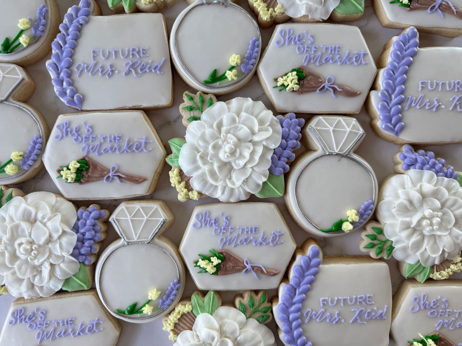 Decorated sugar cookies with purple floral designs and white accents arranged in a pattern.