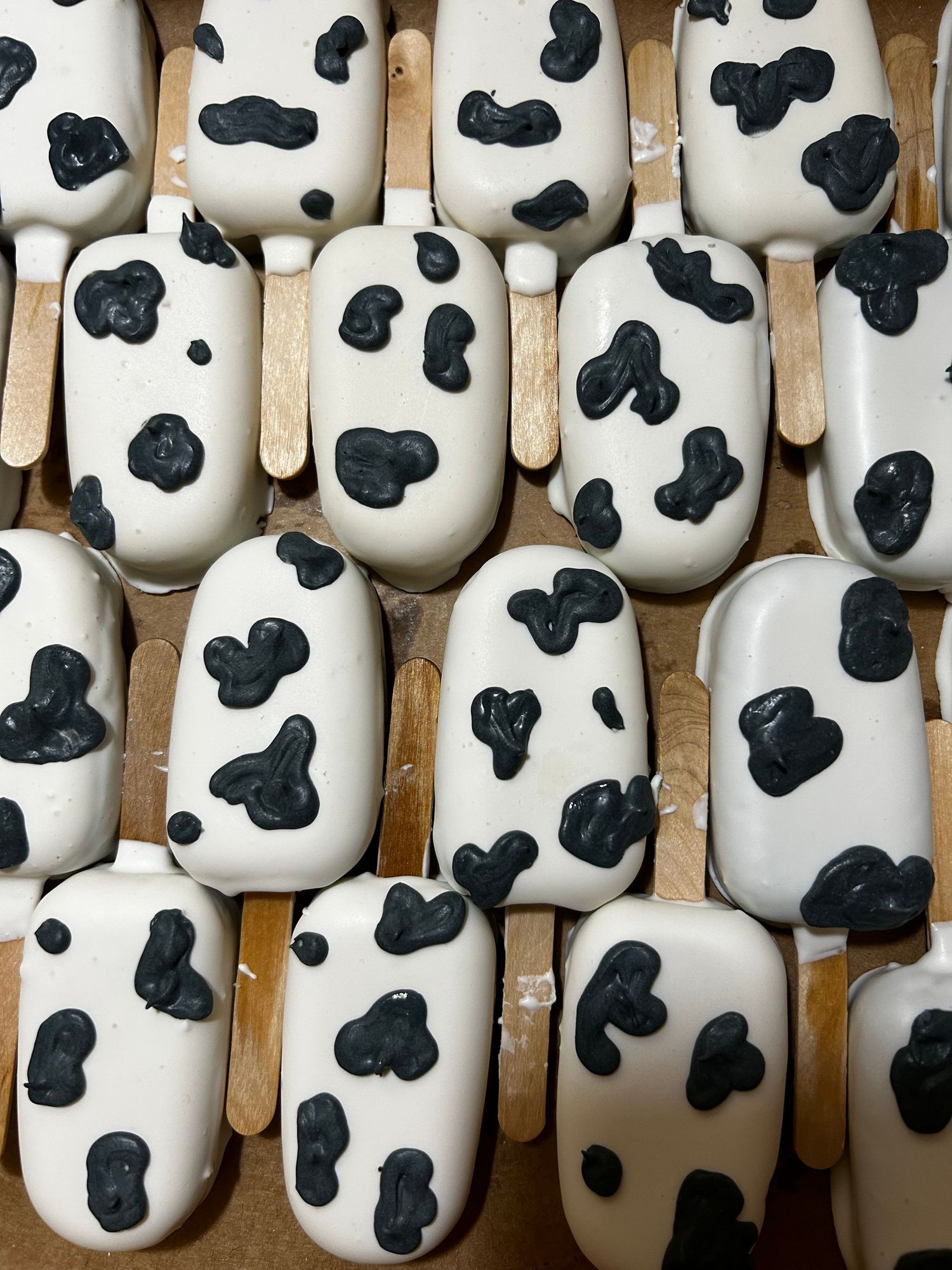 White chocolate-dipped cake pops decorated with black spots in a cow print pattern.