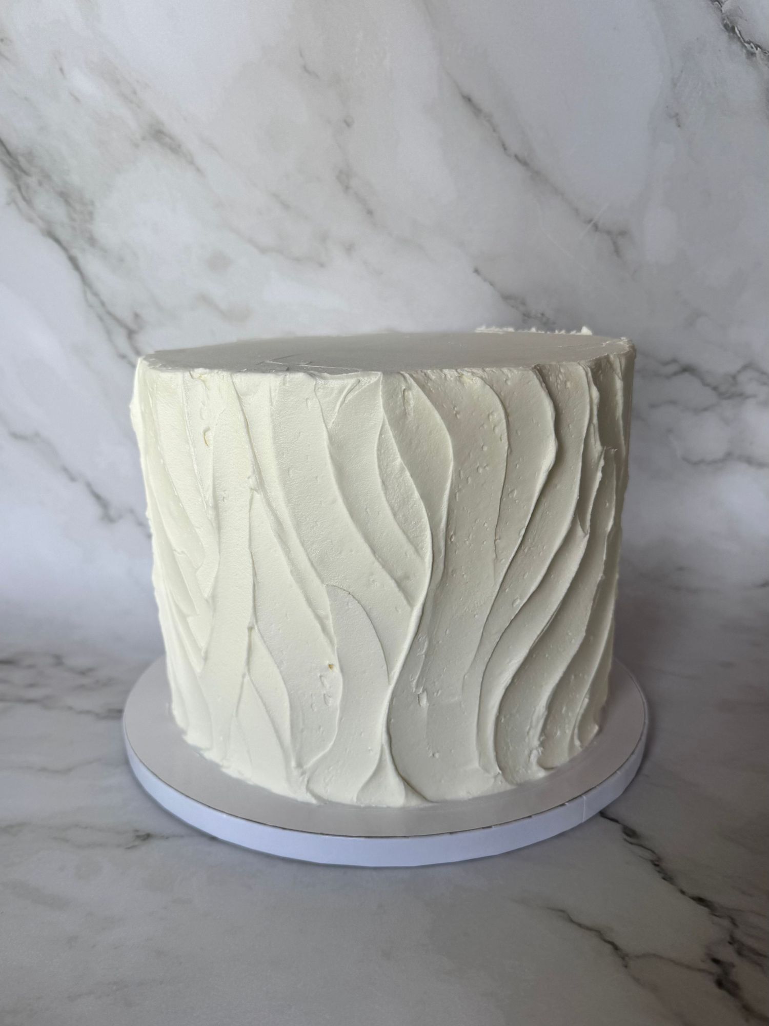 Plain white cake with textured vertical lines in buttercream frosting.