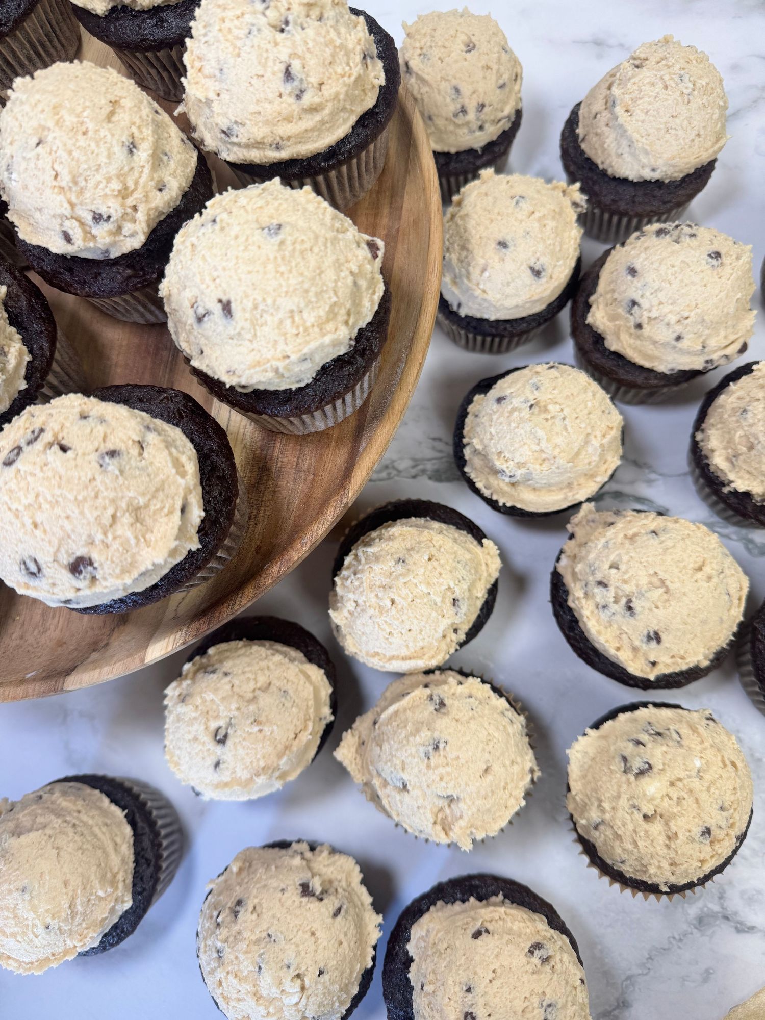 Chocolate cupcakes topped with creamy cookie and cream frosting arranged in rows on a marble surface.