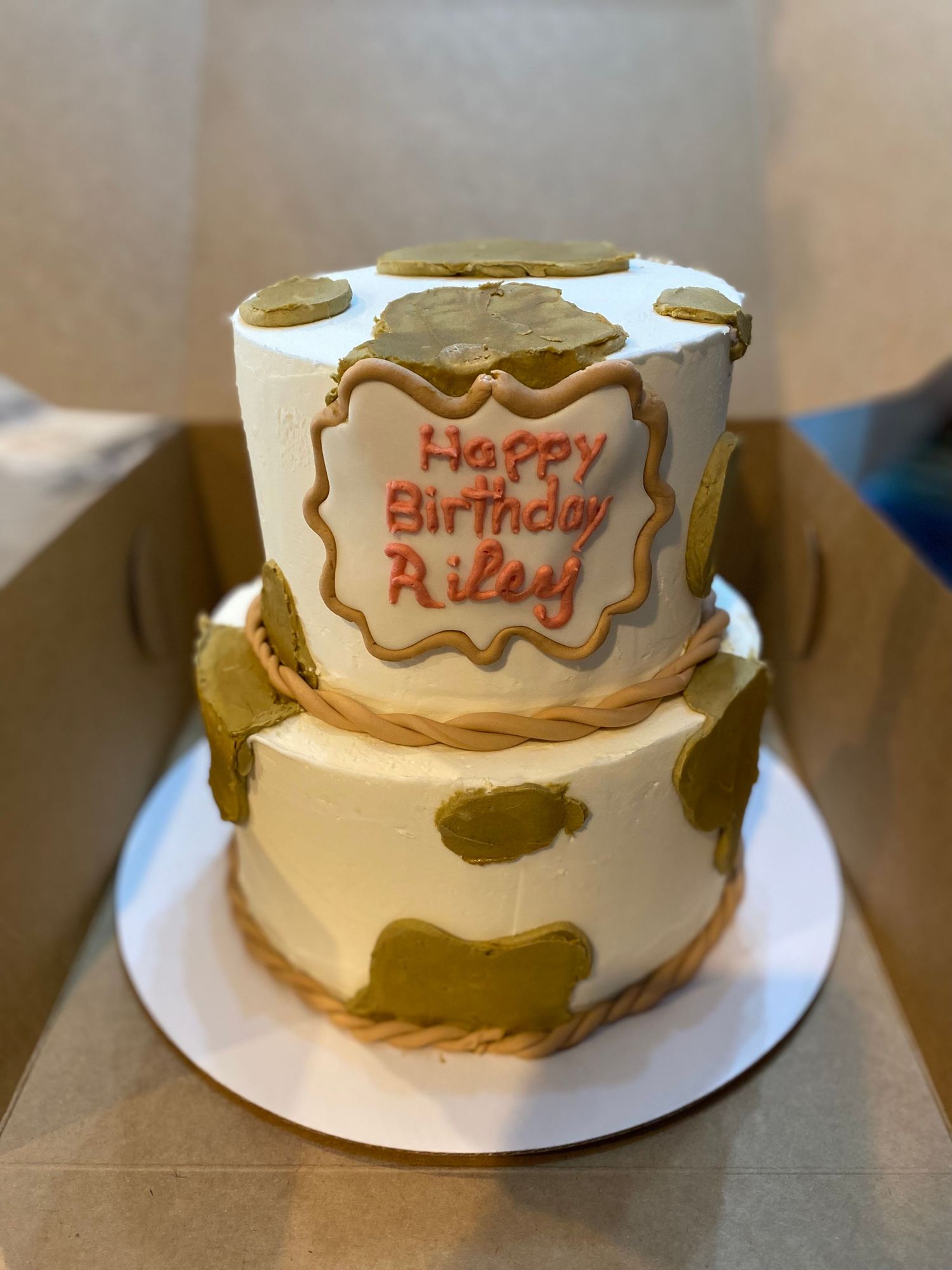 White birthday cake with brown cow print pattern and decorative name plate.