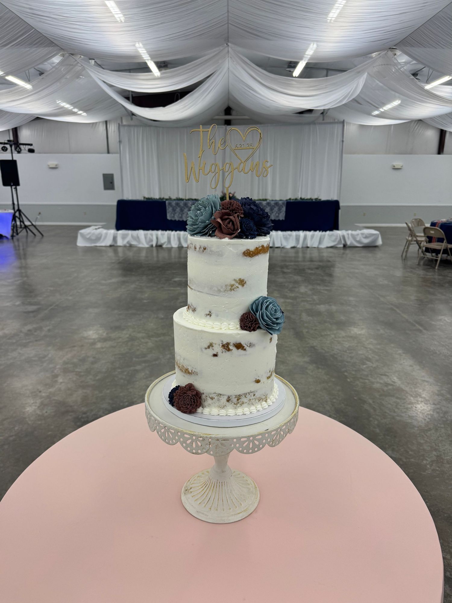 Elegant white wedding cake displayed on a pink table in a spacious reception venue.