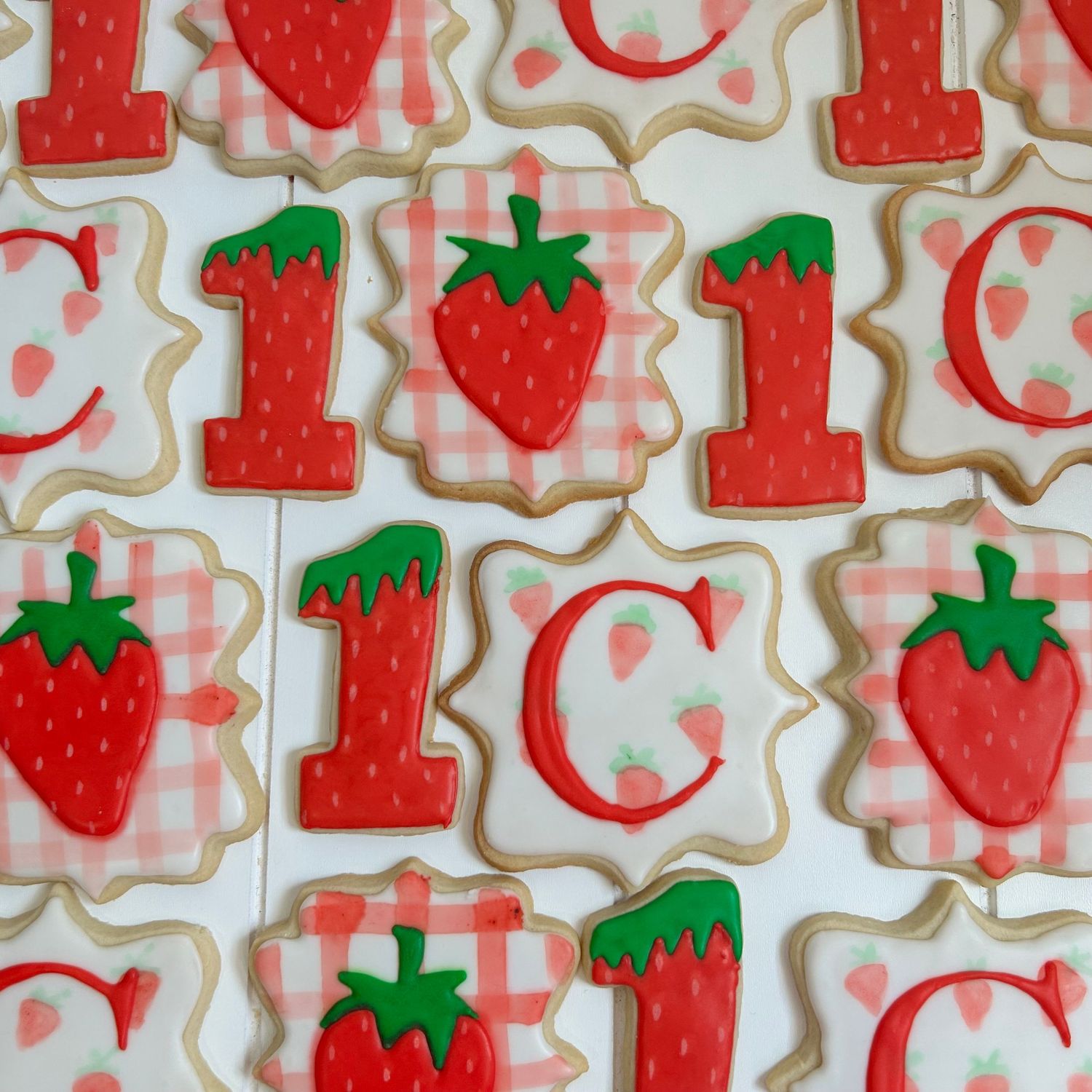 Red strawberry-shaped sugar cookies with detailed icing decorations laid out in rows.