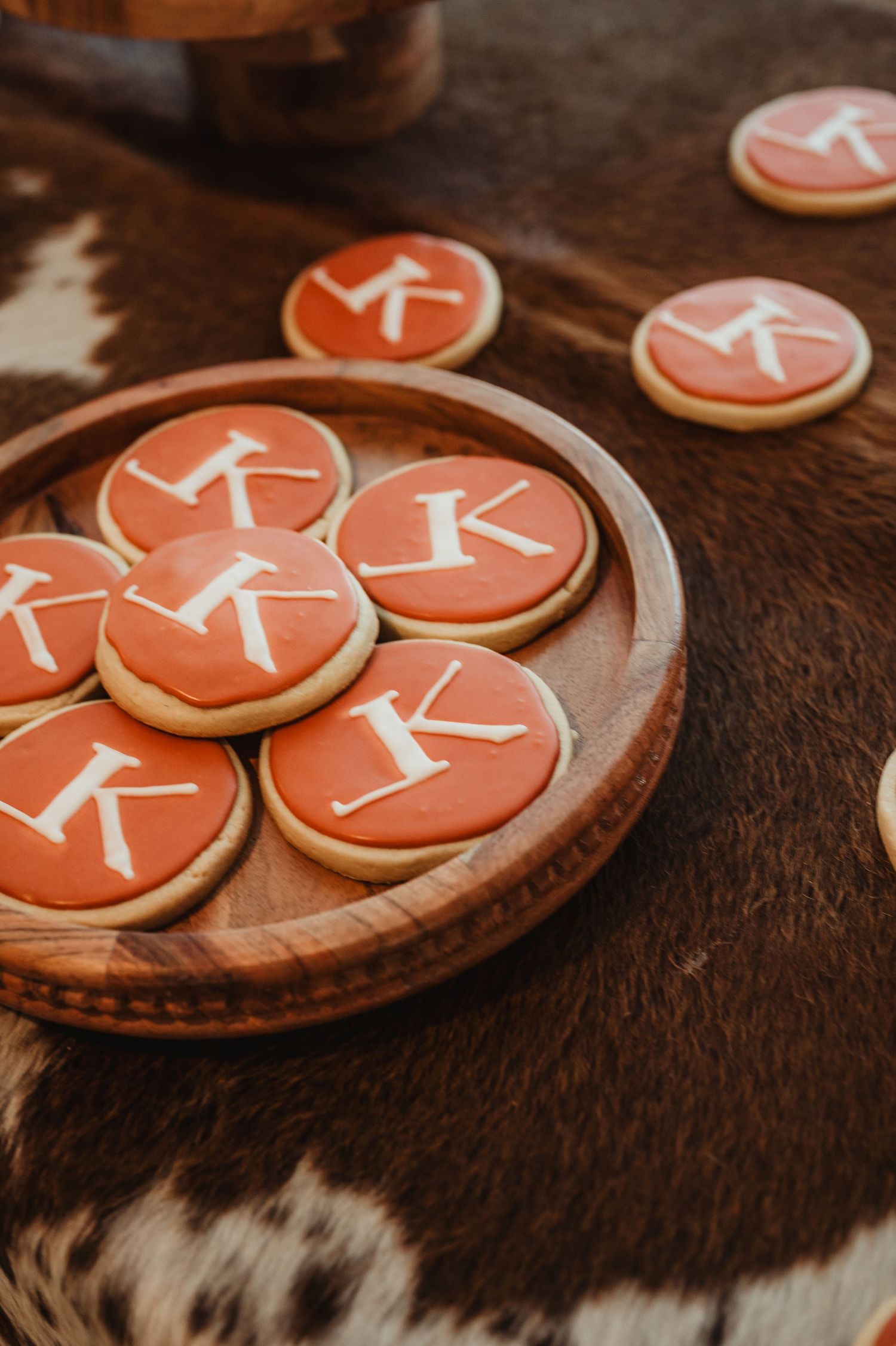 Coral colored monogram cookies with white letter K displayed on a wooden platter.
