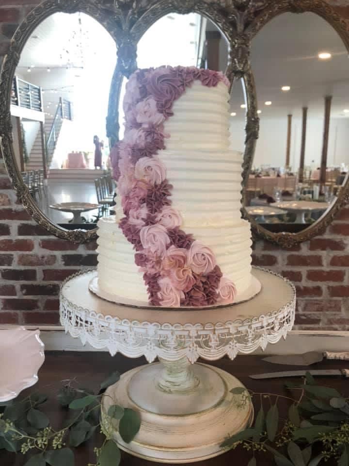 White wedding cake decorated with cascading pink roses on an ornate glass pedestal stand.