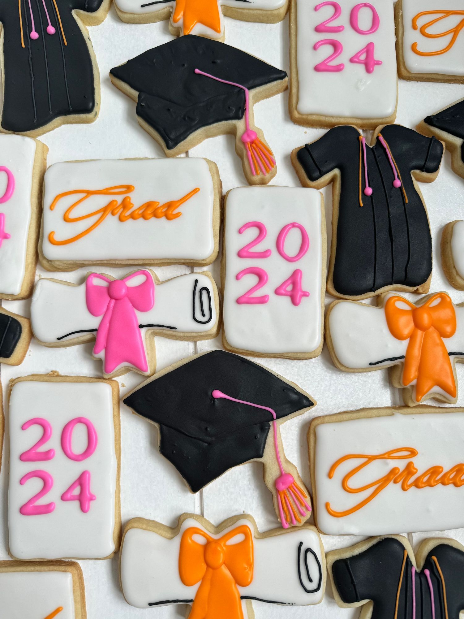 2024 graduation cookies decorated with caps, gowns, and pink and orange bows.