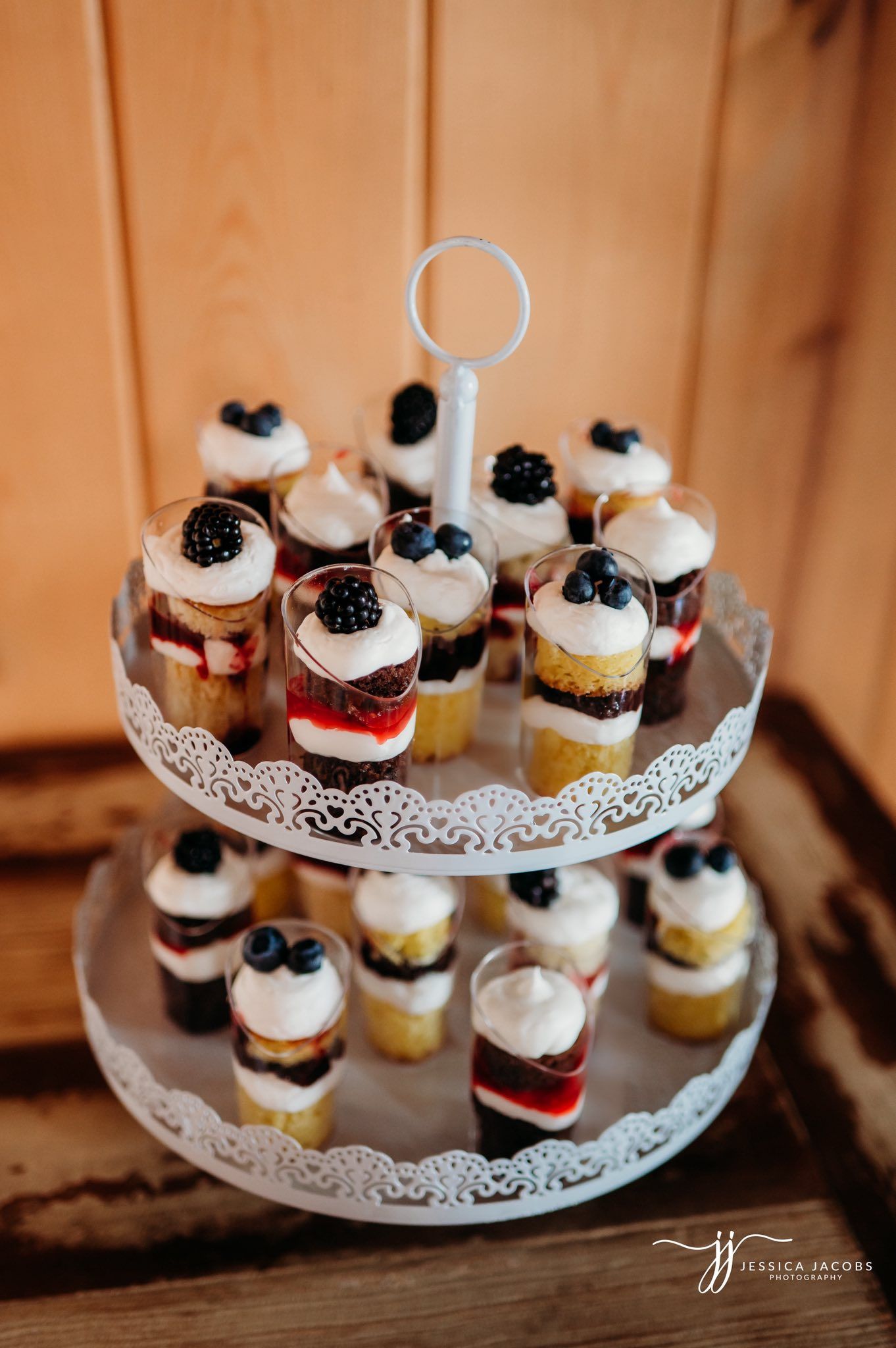 Two-tiered dessert stand displaying mini cupcakes topped with berries and whipped cream.