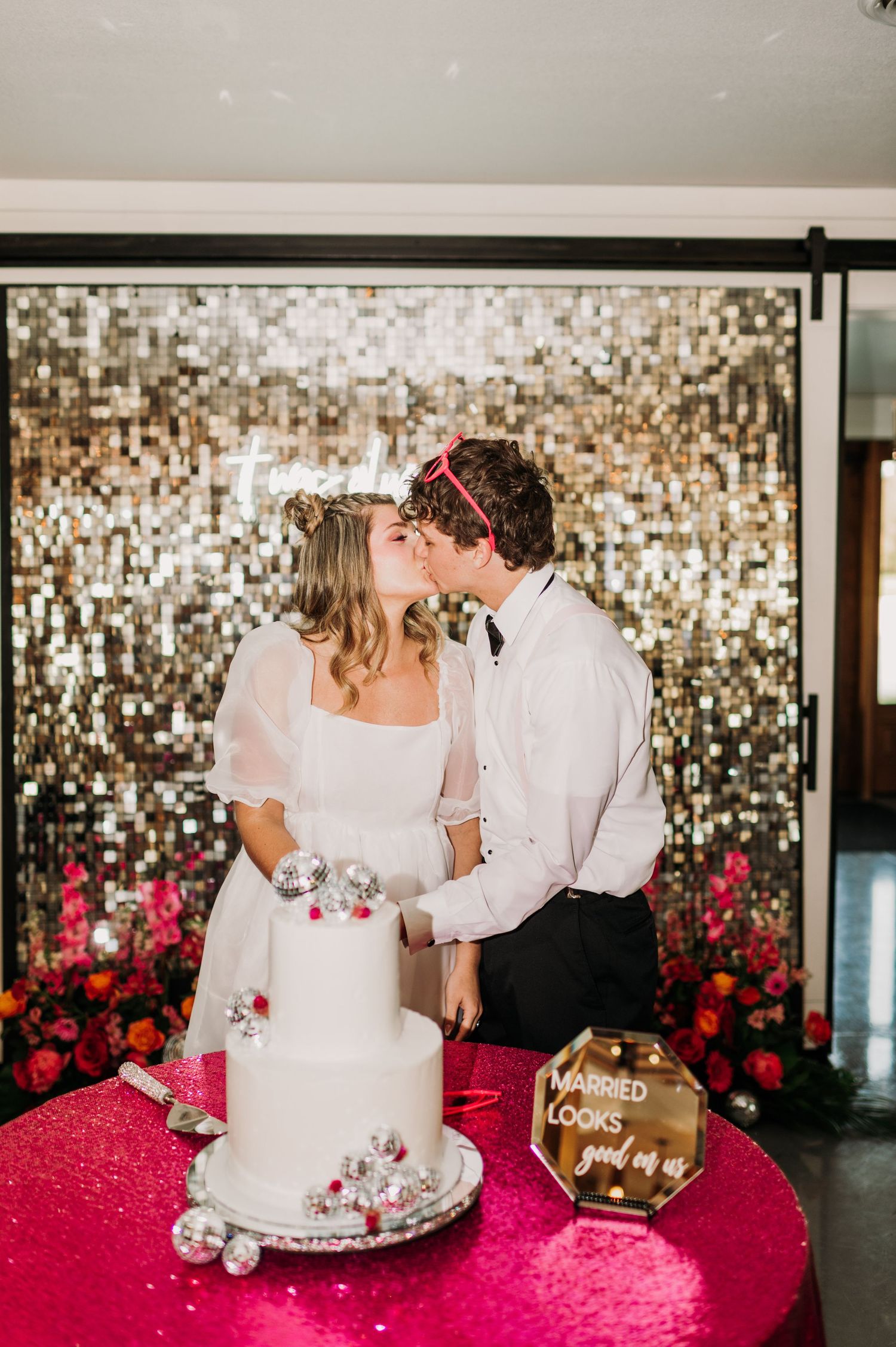Wedding celebration scene with sparkly backdrop and pink floral decorations.