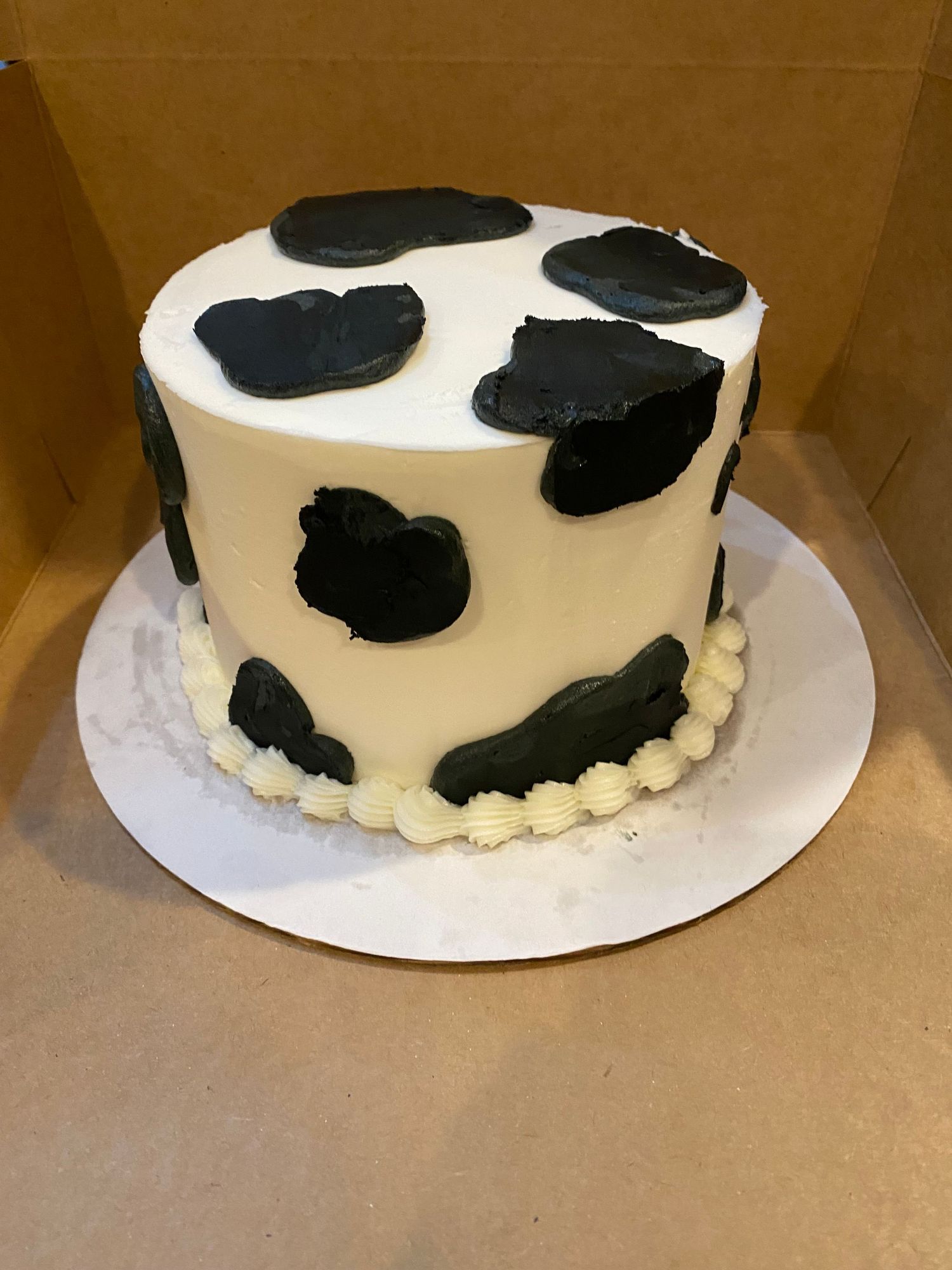 A white round cake decorated with black cow spots and a pearl border.