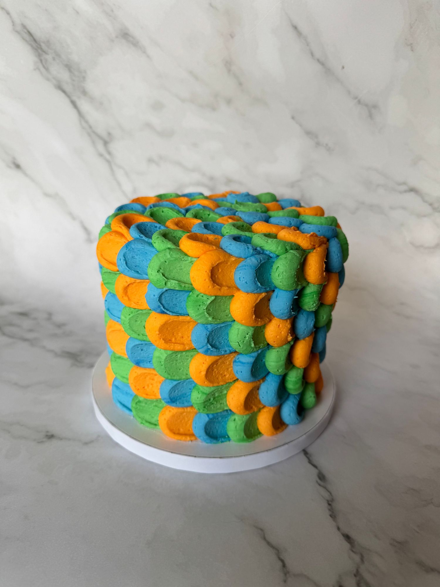 Colorful petal-textured cake with blue, orange and green frosting on marble countertop.