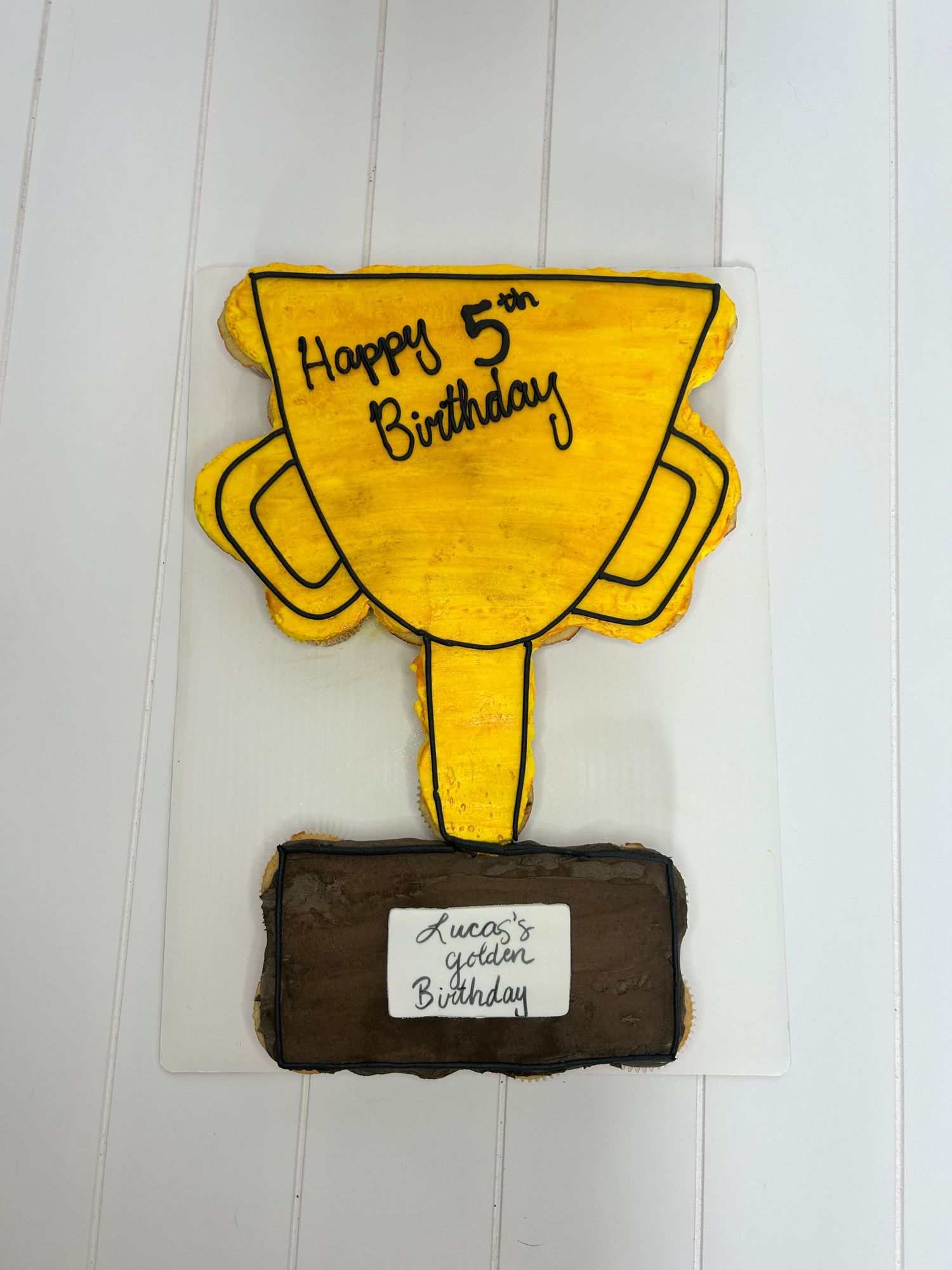 A yellow trophy-shaped cake with Happy Birthday text on a chocolate base.