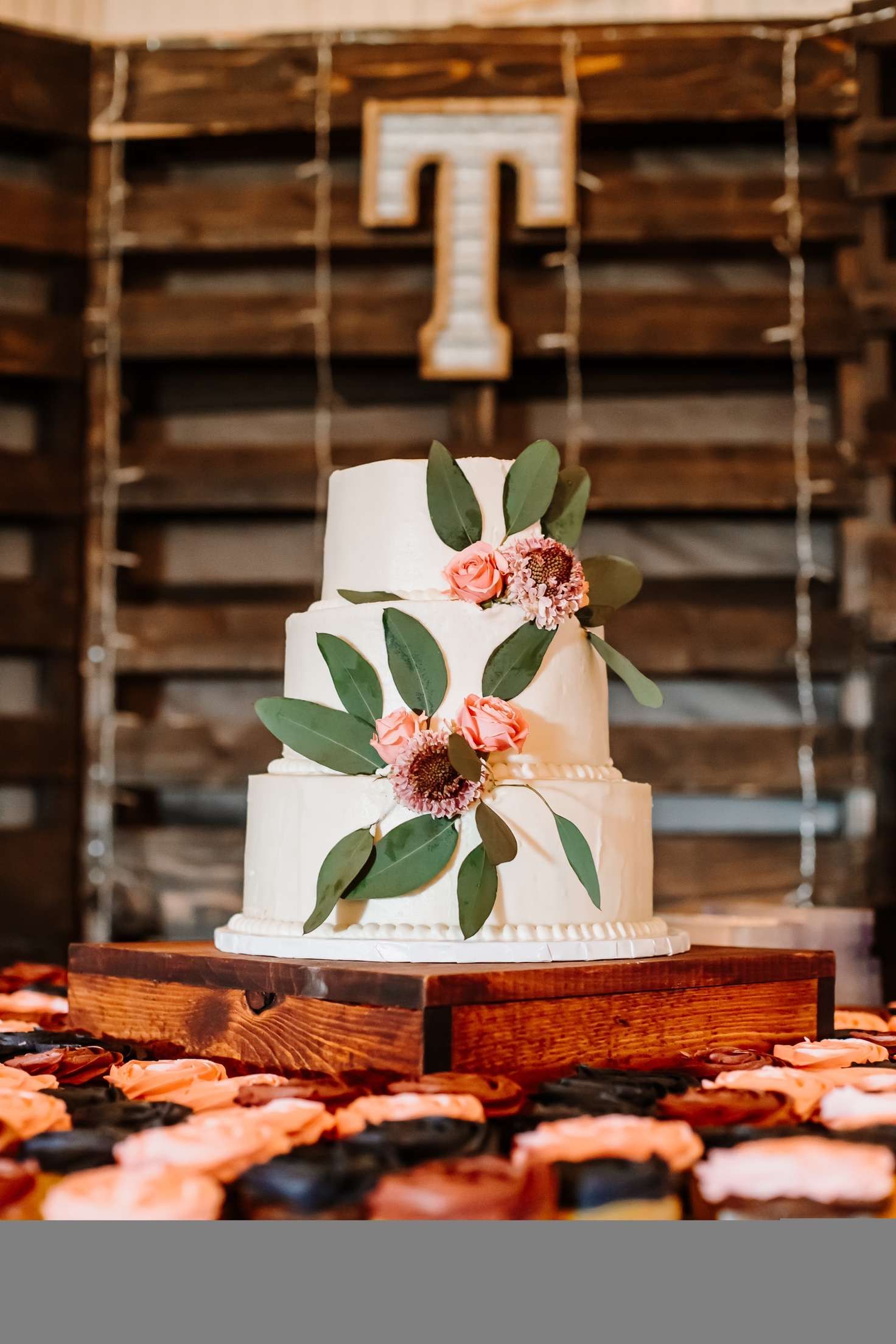 Rustic wedding cake with white frosting and floral decorations displayed on wooden cake stand.