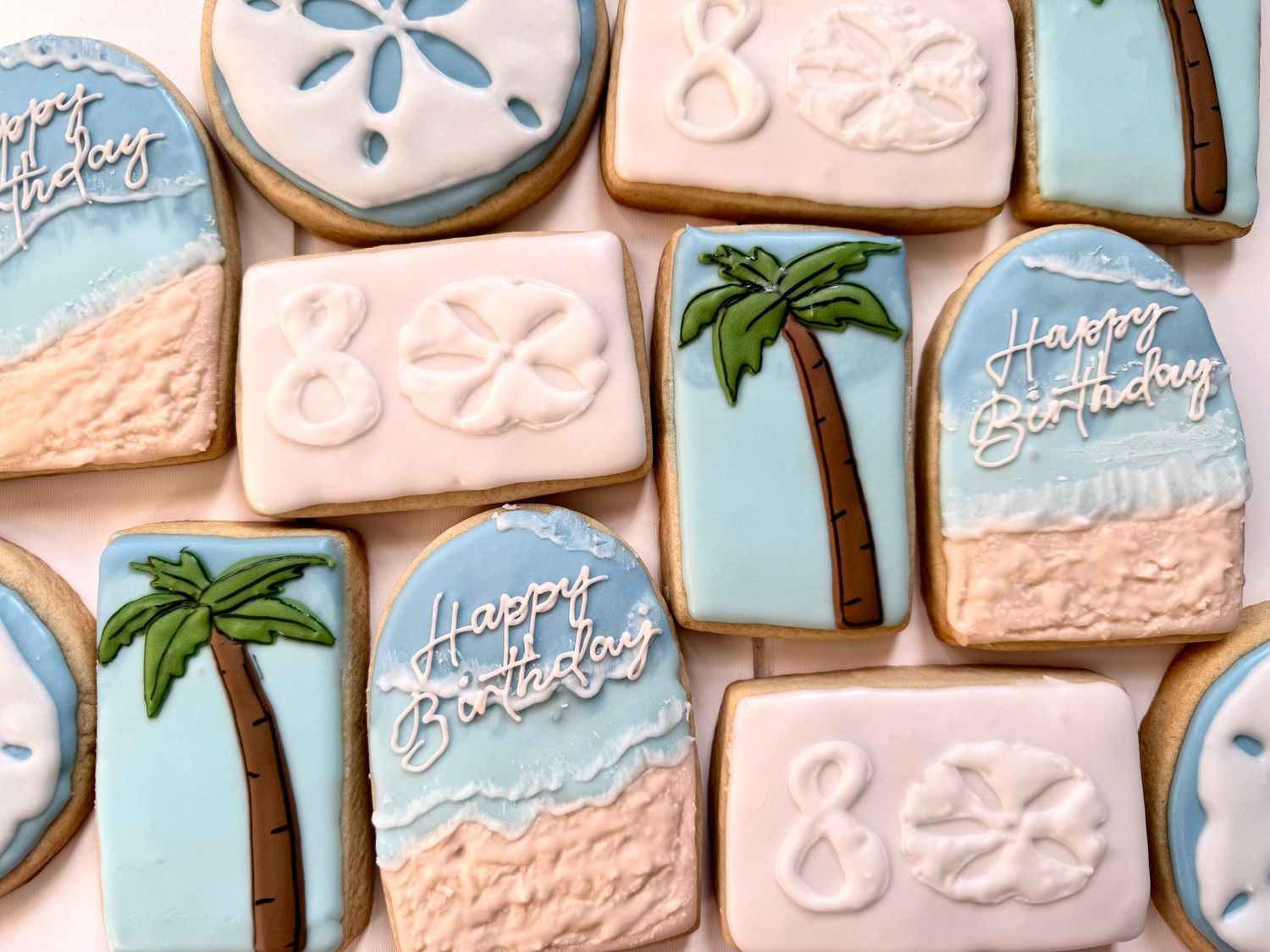 Tropical themed sugar cookies decorated with palm trees and blue waves in pastel colors.