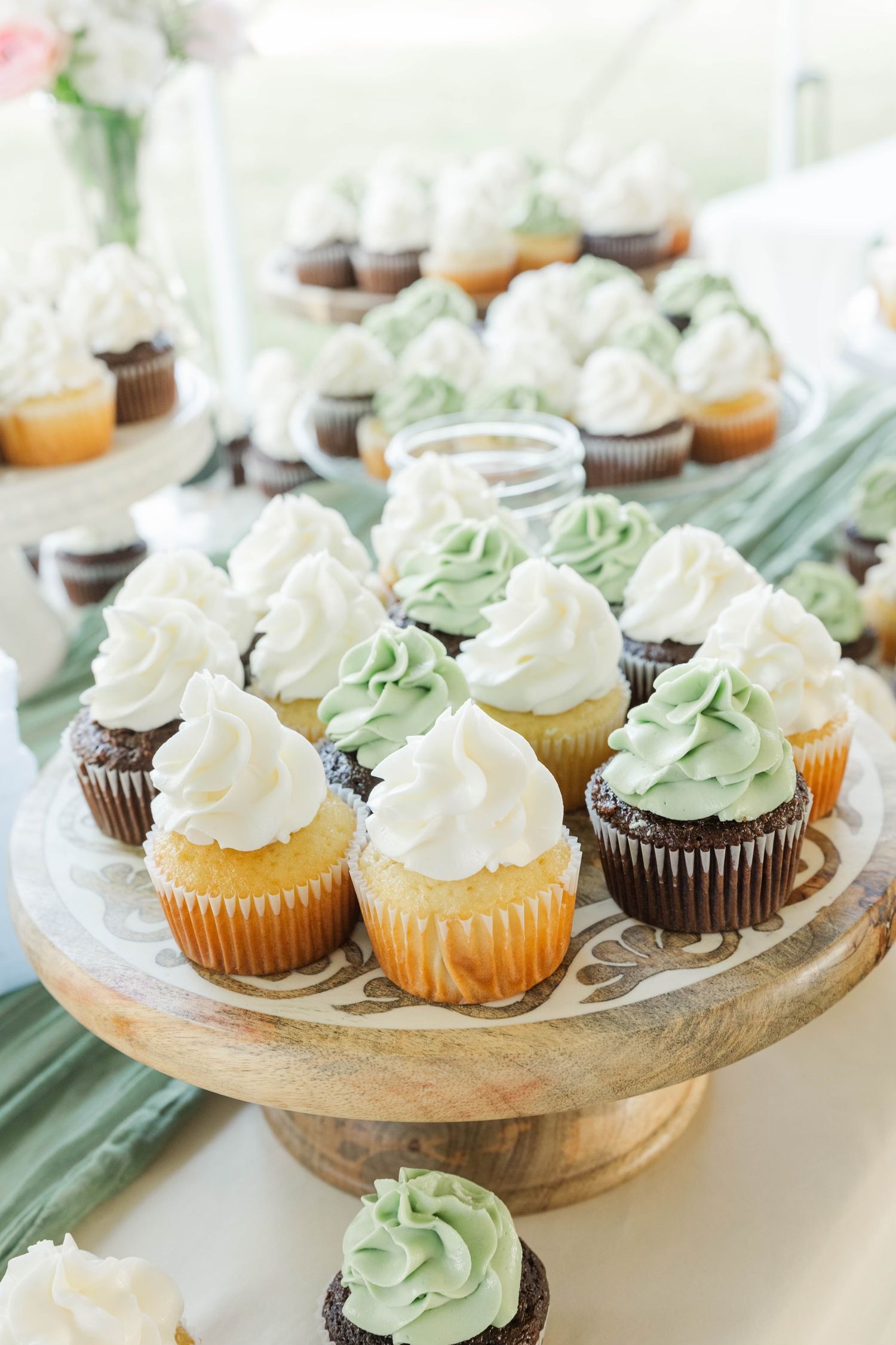 Cupcakes with white and mint green frosting displayed on wooden cake stands.