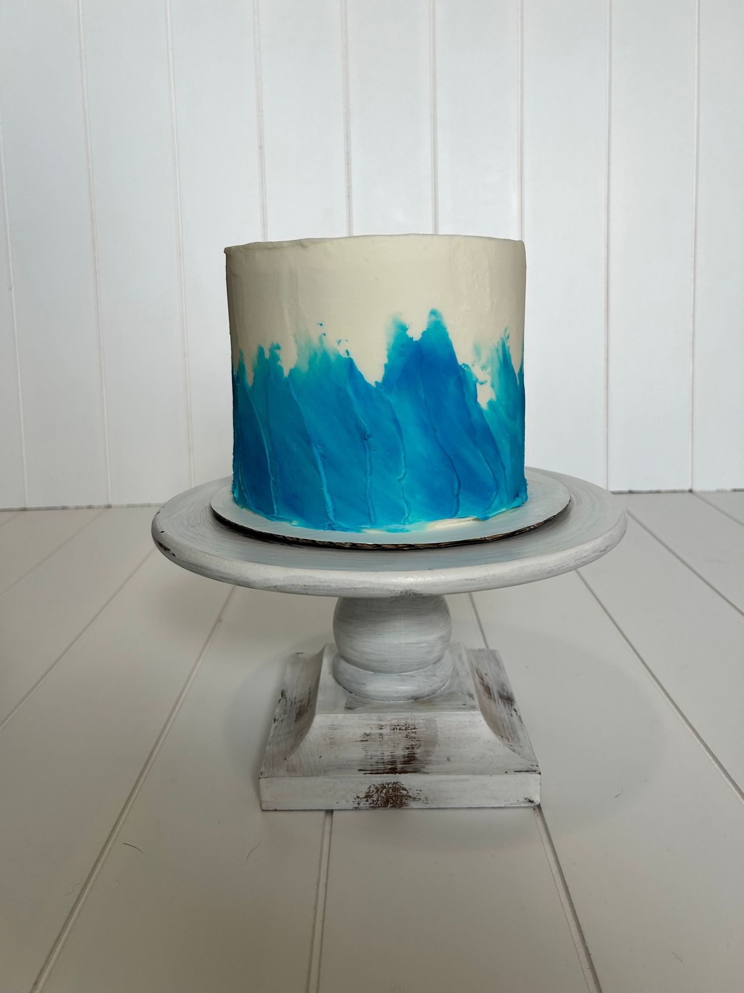 White cake with blue watercolor effect frosting on a distressed white pedestal.