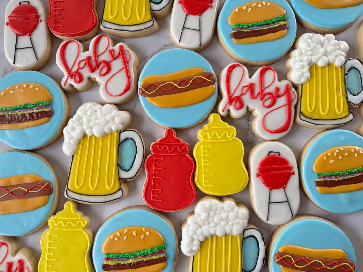 Colorful decorated sugar cookies featuring hamburgers, beer mugs, and BBQ grill designs.