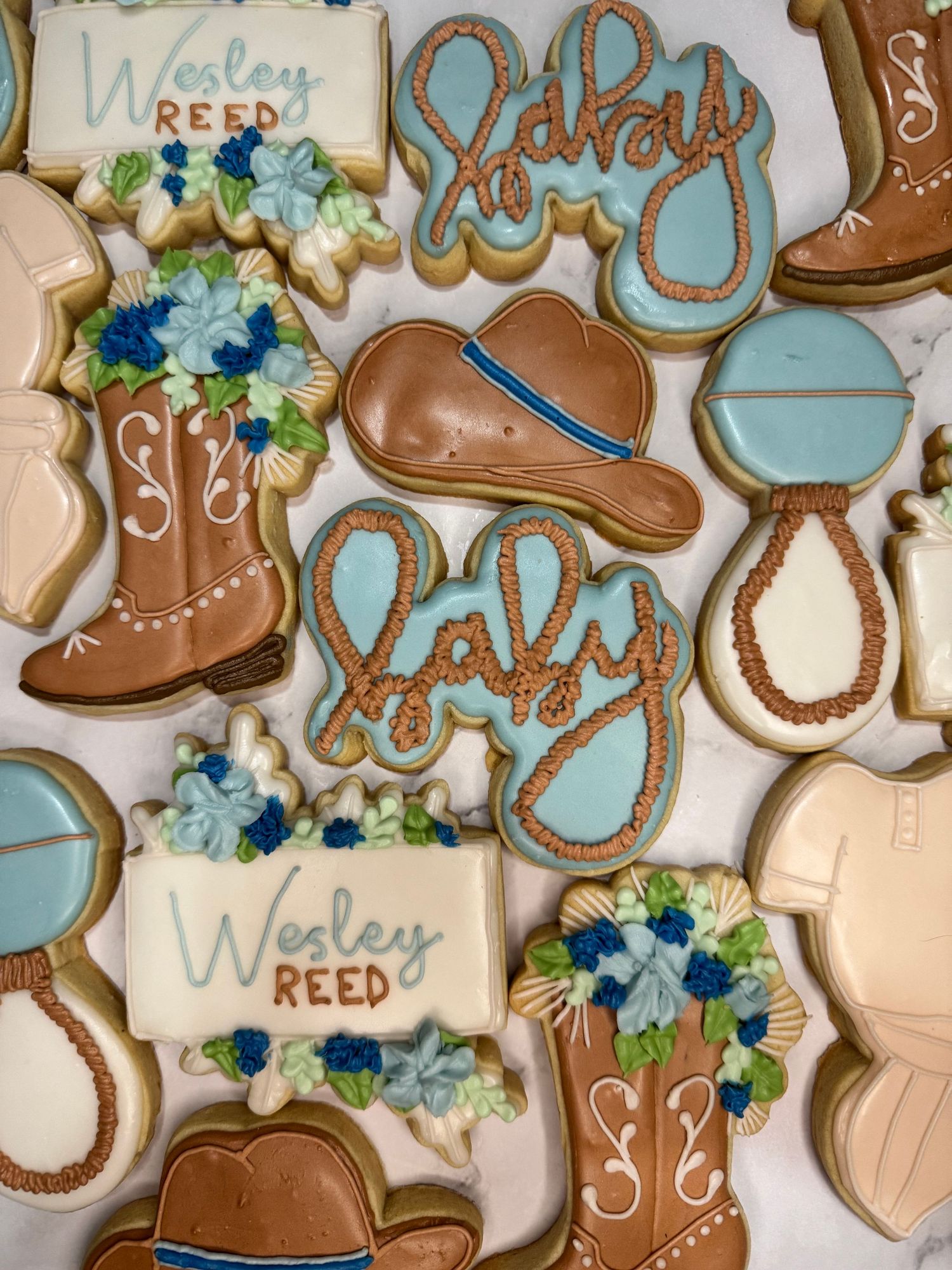 Western-themed sugar cookies decorated with cowboy boots and blue floral designs.