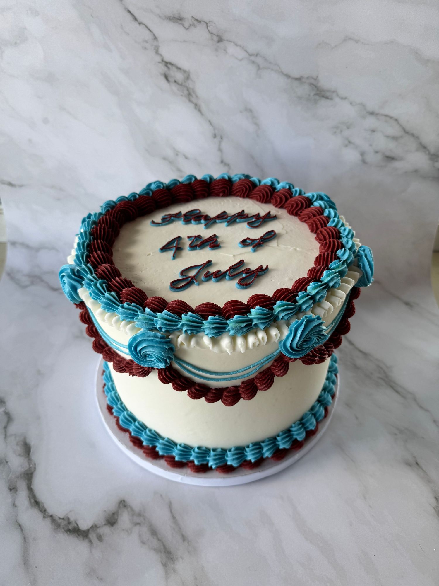 Round cake with white frosting and alternating blue and burgundy piped decorations.