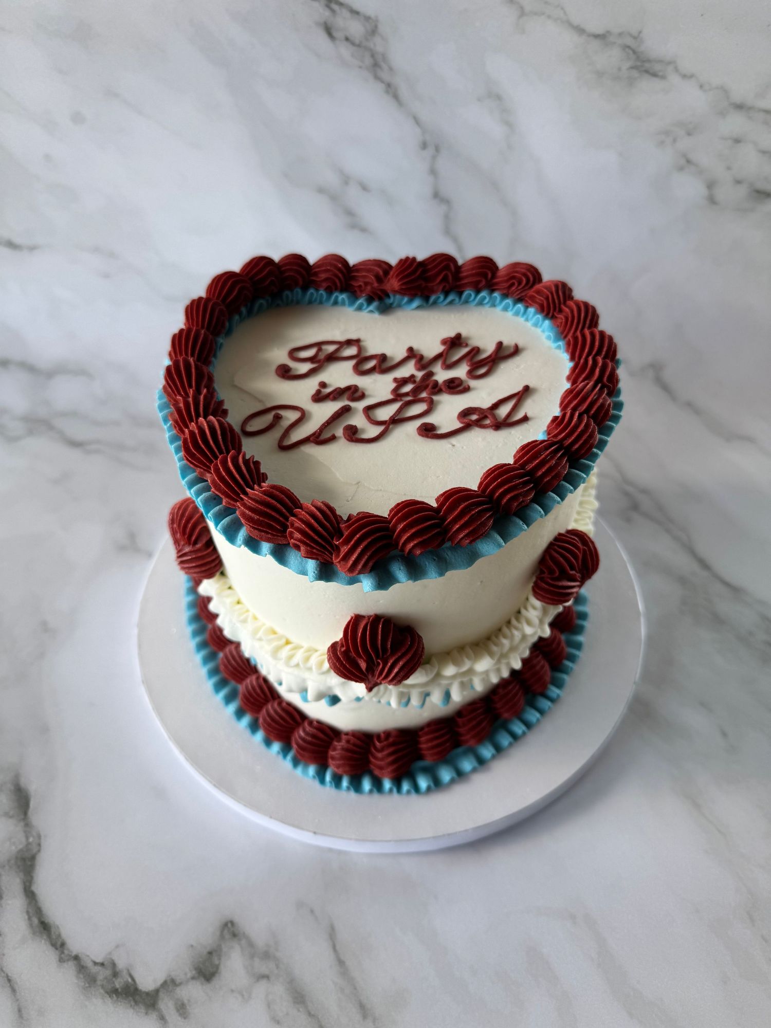 White frosted cake with burgundy and turquoise piped border details.