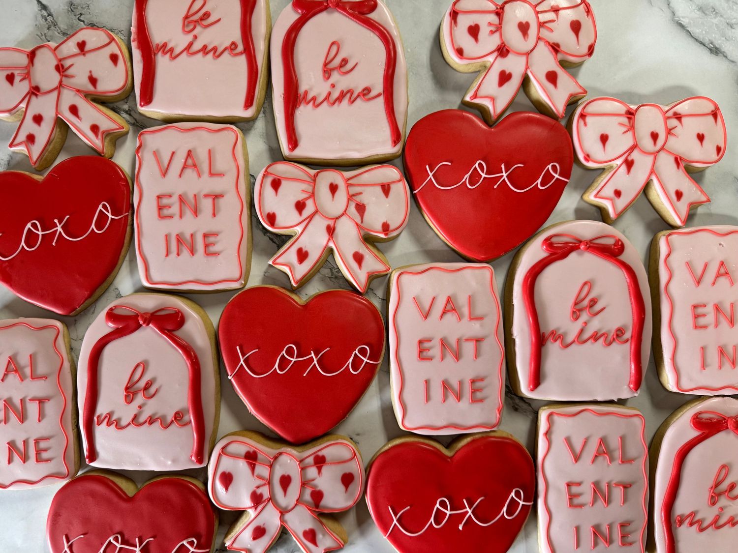 Decorated Valentine's Day cookies with red and pink icing arranged in rows featuring hearts and XOXO designs.